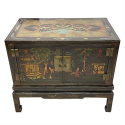 Pair of early 20th century Chinese ebonised and lacquered wood cabinets, the top decorated with dragons over lapping waves within a gilt patterned panel, the surrounding band decorated with Chinese symbols and flowerheads, enclosed by two doors each with village scenes with pagodas, figures and trees, the panelled sides decorated with a figure riding a dragon on stands with gilt decorated 