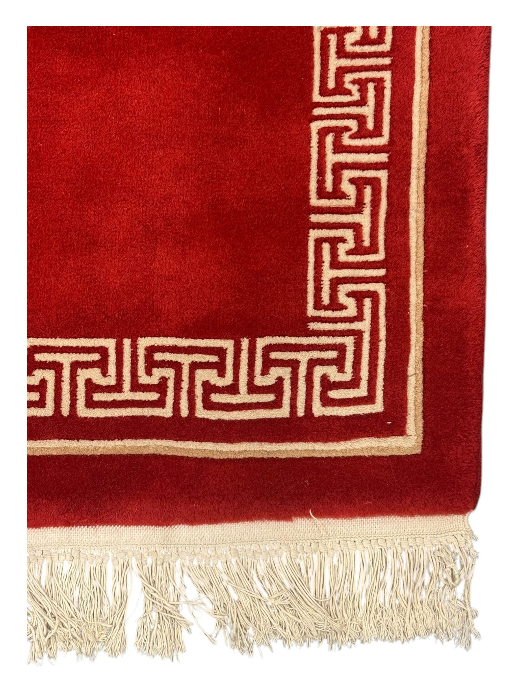 Chinese washed woolen red ground rug, central circular dragon motif in ivory, framed by a decorative Greek key border in matching ivory tones, finished with fringed ends