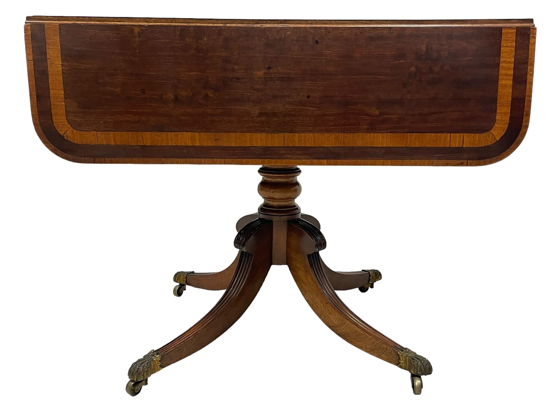 Early 19th century mahogany Pembroke table, rectangular drop-leaf top with rounded corners inlaid satinwood bands, single end drawer and opposing false drawer, turned pedestal on four acanthus carved and reed moulded splayed supports, cast brass cups and castors 