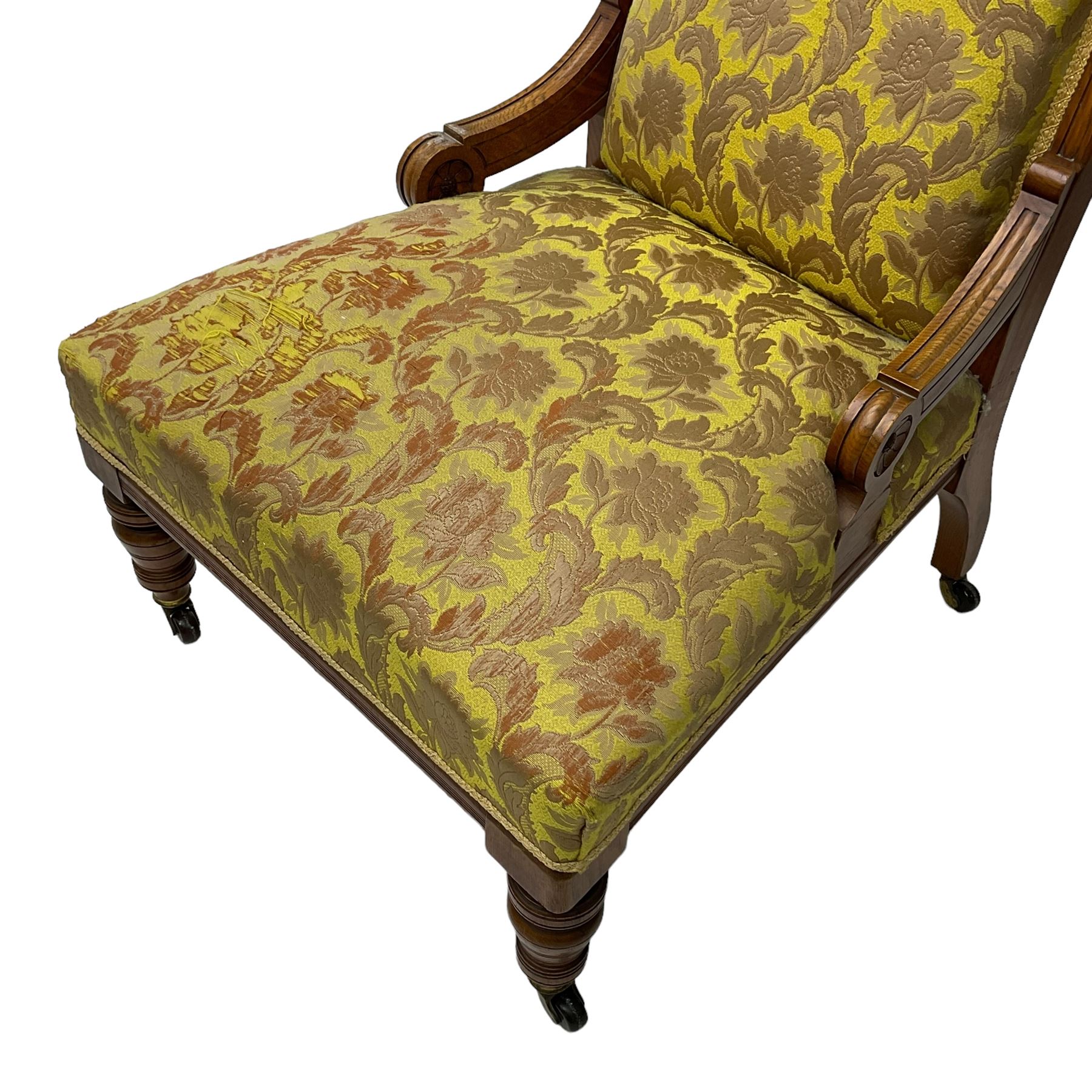 Late Victorian oak nursing chair, moulded frame with flower head carved roundels, upholstered in floral pattern fabric, on turned front feet with brass and ceramic castors 