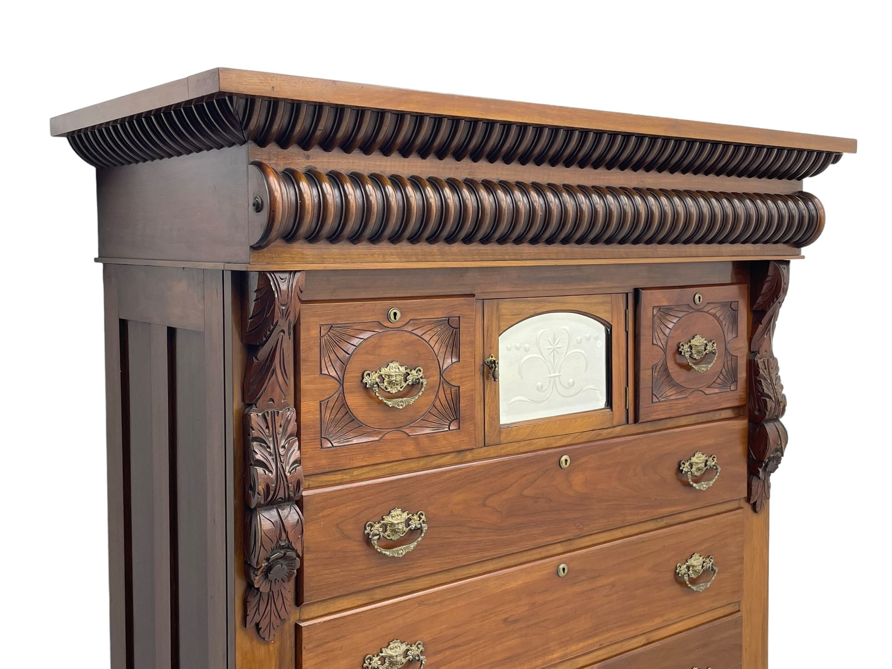 Late Victorian walnut Scotch chest, projecting cornice with turned quarter column mounts over matching half column to frieze, fitted with two upper short drawers with central cupboard, bevelled mirror glazed cupboard door, four graduating drawers below, foliage and flower head carved brackets to the uprights, panelled sides, chamfered plinth on turned feet