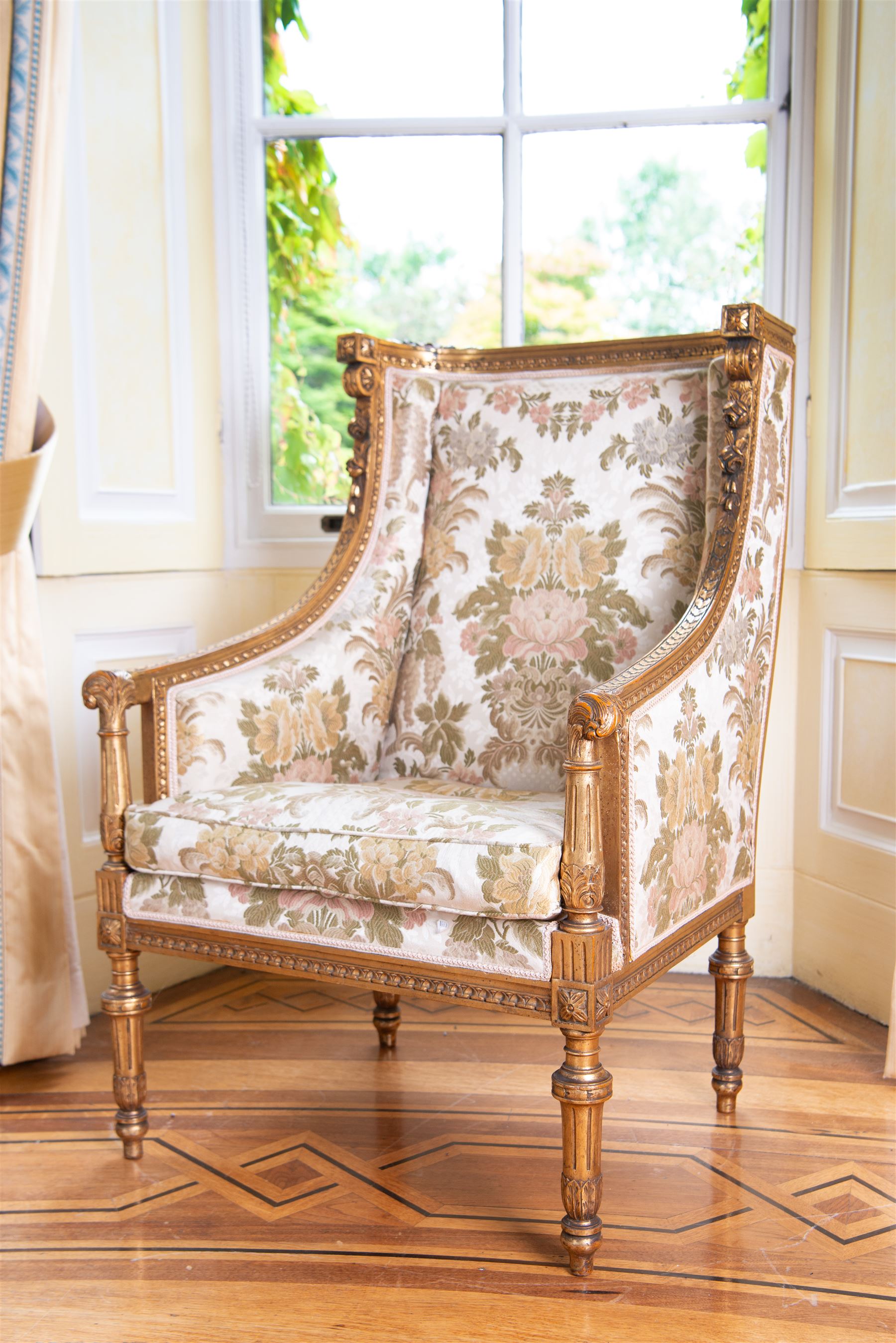 Late 19th century French gilt wood and gesso enclosed armchair, the cresting carved with floral bouquets over foliate moulding, upholstered in floral pattern fabric with repeating pattern, down-swept arms with scrolled acanthus leaf terminals, on turned and fluted feet carved with foliage 