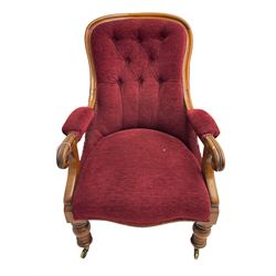 Victorian mahogany framed open armchair, upholstered in buttoned red fabric, the arm terminals carved with scrolls, on turned front supports with brass cups and castors