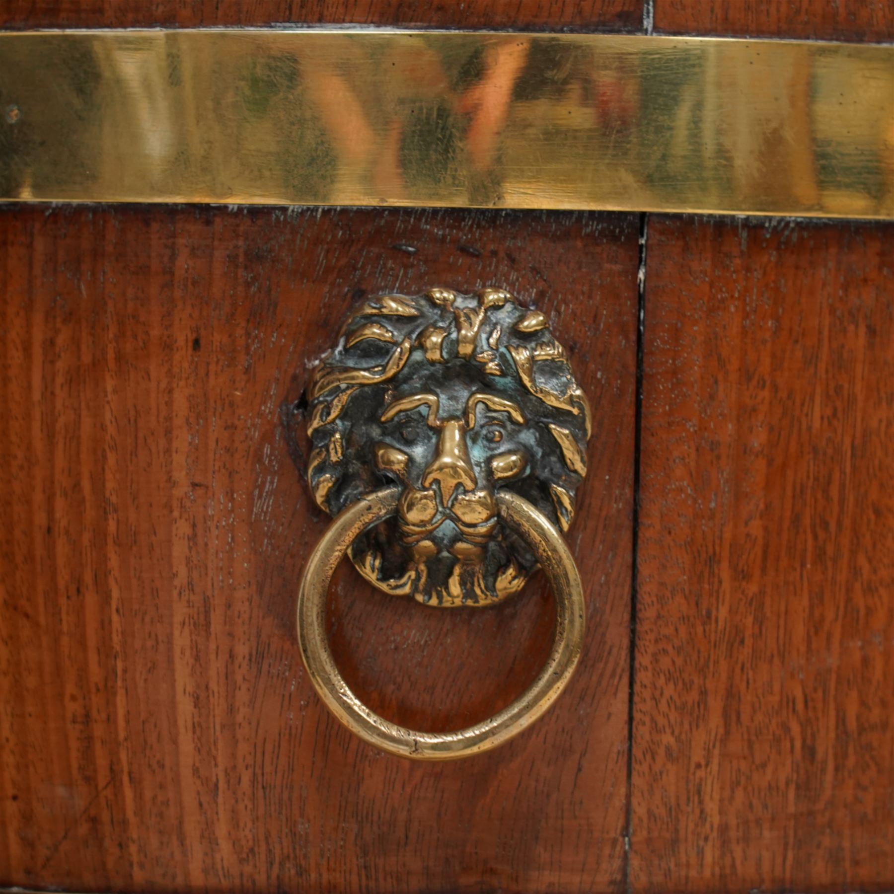 George III Chippendale design brass bound mahogany wine cooler of oval form, the coopered body enclosed by two brass brands, with lead liner to interior, fitted with twin lion mask ring handles, raised on square tapering supports