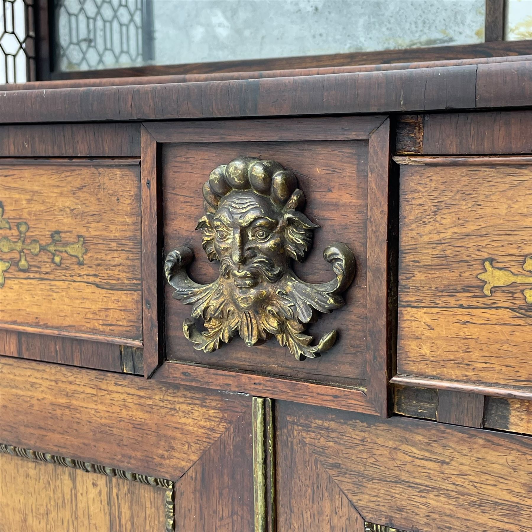 Attributed to John McLean & Son (London: 1770-1825) - Regency rosewood chiffonier, the raised two tier mirrored back on turned brass supports with brass trestle sides, rectangular top with brass stringing over two drawers and central cast brass satyr mask, cock-beaded drawer fronts inlaid with extending stylised foliate brass work, double cupboard below enclosed by panelled doors with cast egg and dart edging, matched brass inlays to the uprights, fitted with internal shelf, on turned compressed bun feet 