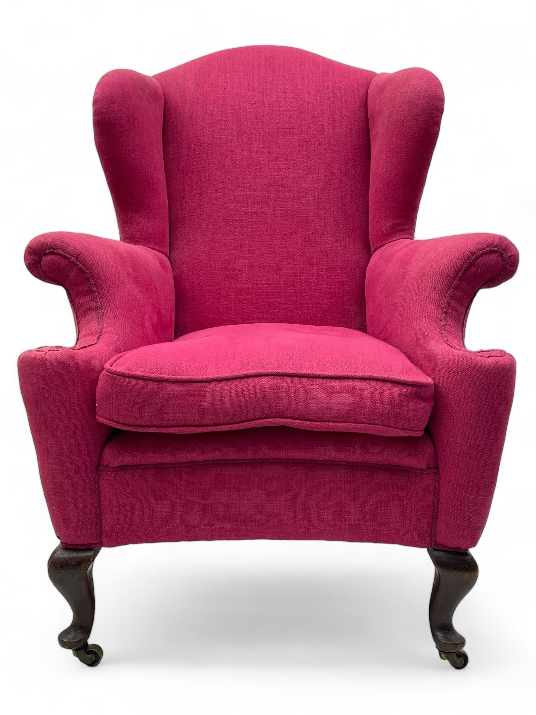 Georgian design hardwood-framed wingback armchair, arched cresting rail over curved wingback, rolled arms on scrolled cushioned supports, reverse bow-front, upholstered in claret red fabric with loose seat cushion, on cabriole front feet and brass castors 