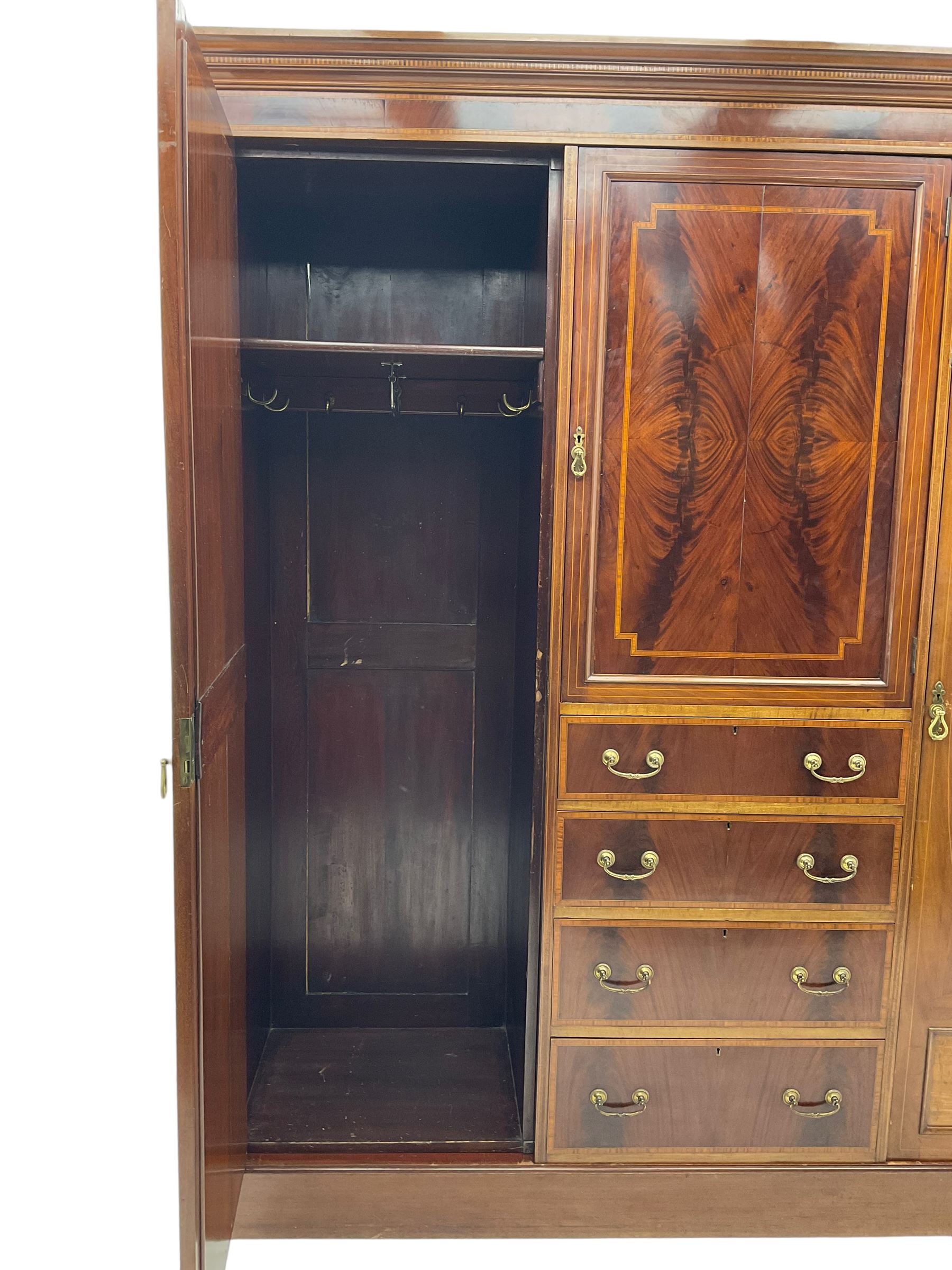 Edwardian inlaid mahogany combination wardrobe, projecting moulded cornice over figured frieze with satinwood banding, the central section fitted with cupboard over four long drawers, figured matched veneers and satinwood bands, flanked by two full height compartments enclosed by bevelled shield shaped mirror doors, satinwood fan inlaid spandrels, on moulded skirt base 