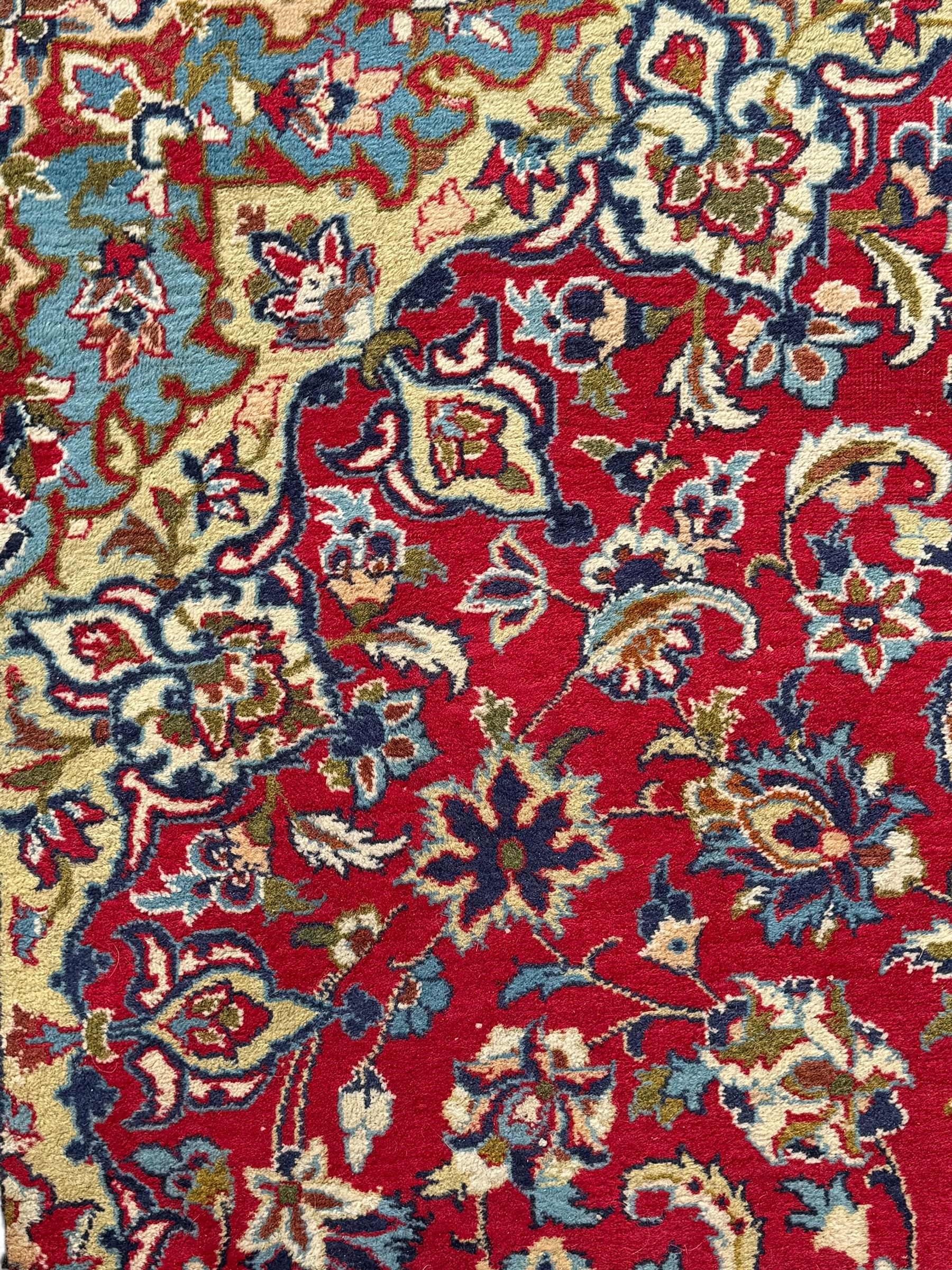 Persian Kashan red ground rug, the field decorated with a central floral medallion surrounded buy scrolling vine motifs and palmettes, the main border featuring a series of stylised floral motifs against a dark blue ground, enclosed by multiple guard stripes with alternating floral and geometric designs