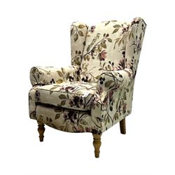 Hardwood-framed wingback armchair, upholstered in cream floral pattern fabric, on turned front feet