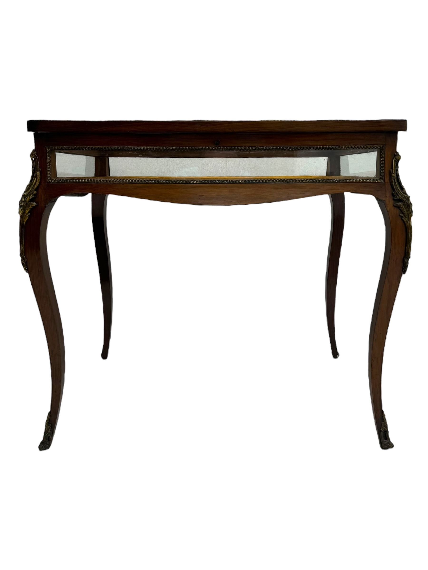 Victorian inlaid rosewood bijouterie table cabinet, shaped form, enclosed by hinged bevel glazed lid with shell and floral inlays, fabric lined interior, glazed sides within foliate cast gilt metal edging, on cabriole supports with floral cast gilt metal mounts and terminal caps 