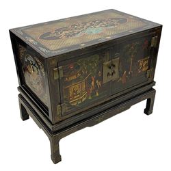 Pair of early 20th century Chinese ebonised and lacquered wood cabinets, the top decorated with dragons over lapping waves within a gilt patterned panel, the surrounding band decorated with Chinese symbols and flowerheads, enclosed by two doors each with village scenes with pagodas, figures and trees, the panelled sides decorated with a figure riding a dragon on stands with gilt decorated 