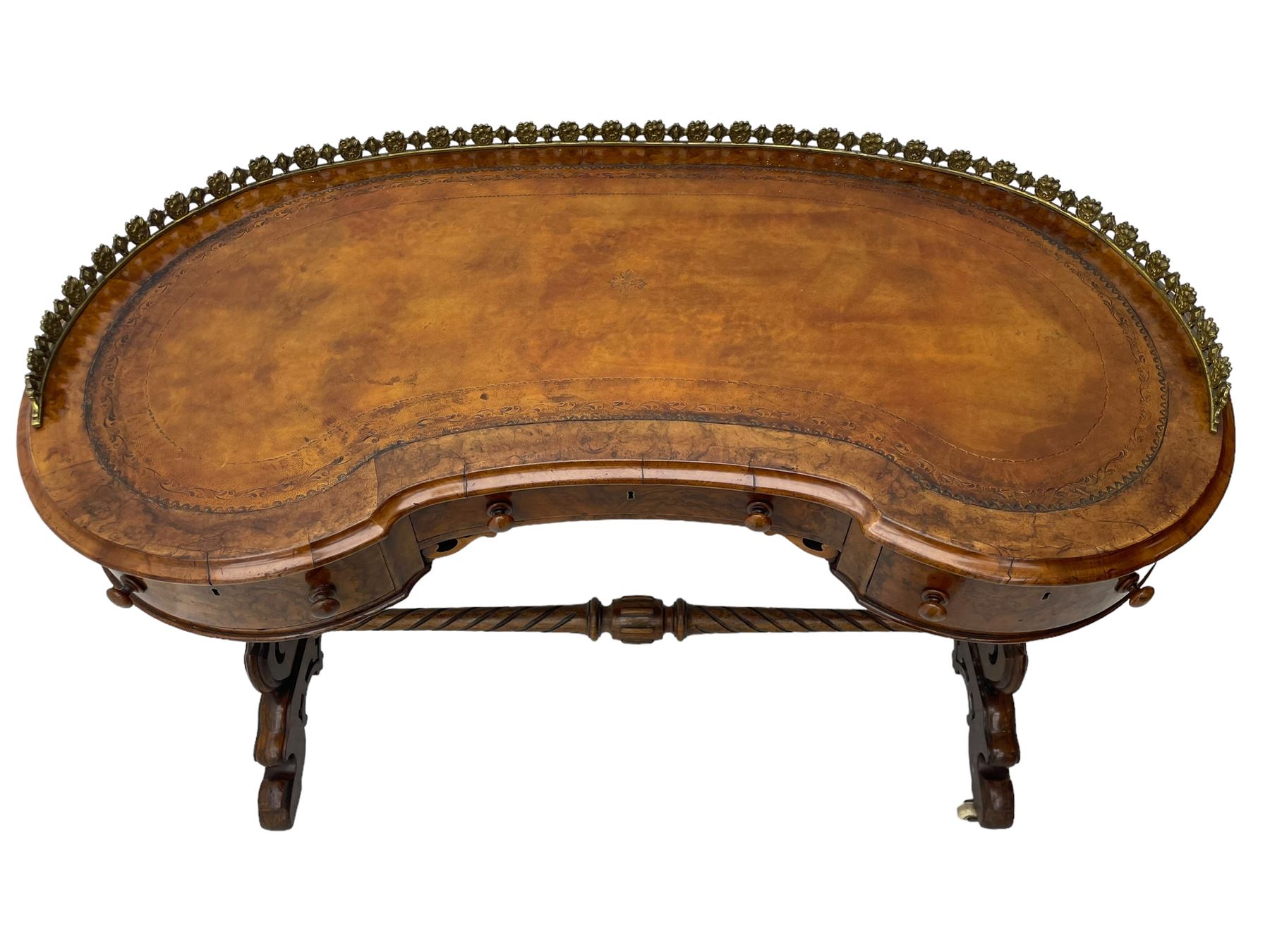 Victorian walnut kidney-shaped writing desk, moulded top with floral cast brass gallery and inset leather writing surface, fitted with three frieze drawers with turned handles, shaped and pierced end supports on raised platforms terminating to splayed feet, united by twist turned and lobe carved stretcher, brass and ceramic castors 