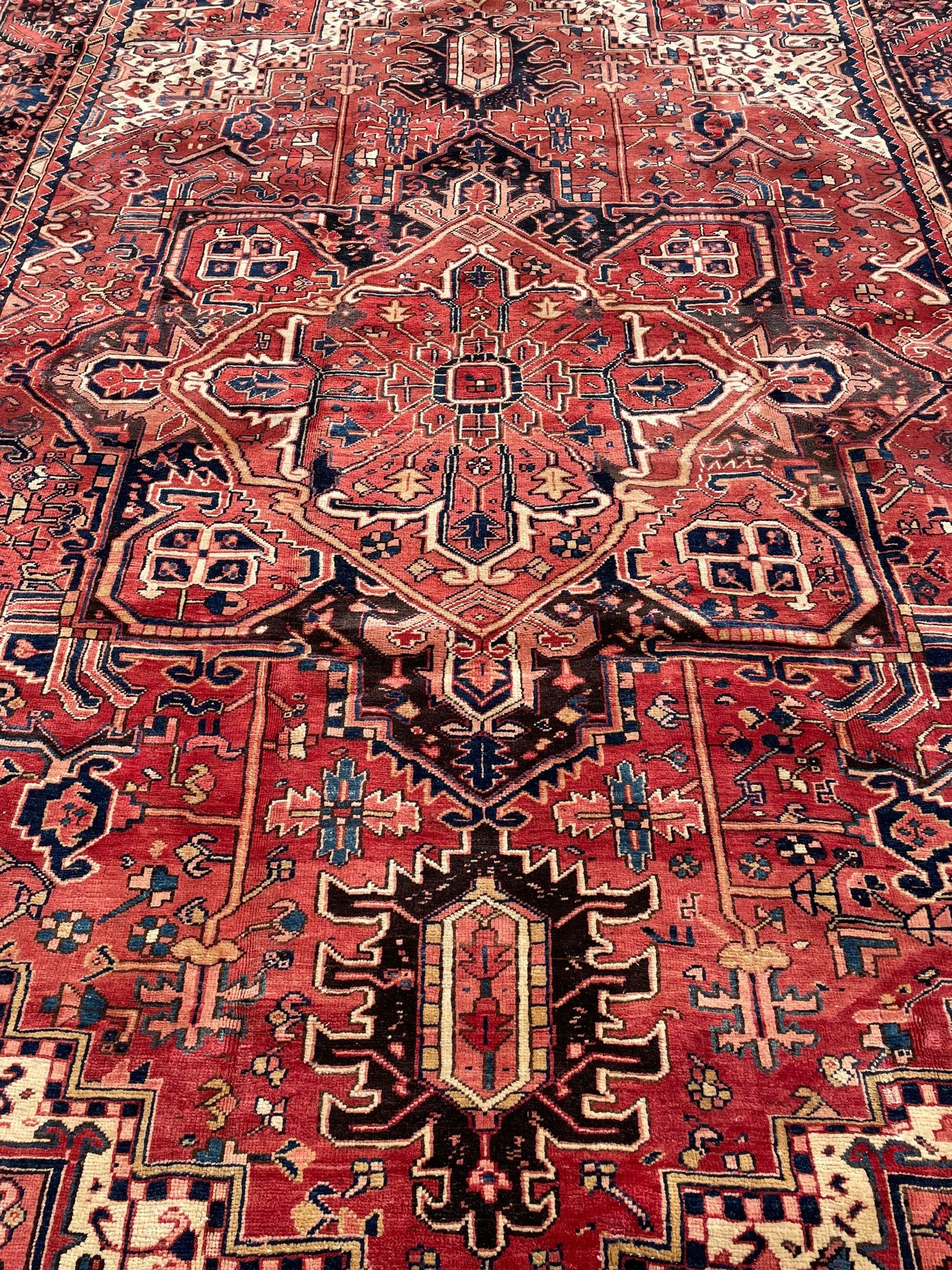 Persian Heriz red ground carpet, large central eight point medallion with projecting palmettes surrounded by small geometric motifs, decorated profusely with hooks, rosettes and animals, the busy border decorated with stylised foliate motifs within guard stripes 