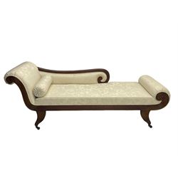 Regency design mahogany chaise longue, scrolled arms with carved rosette details, upholstered in cream damask fabric with bolster cushion, reeded frame supported by turned legs on brass castors