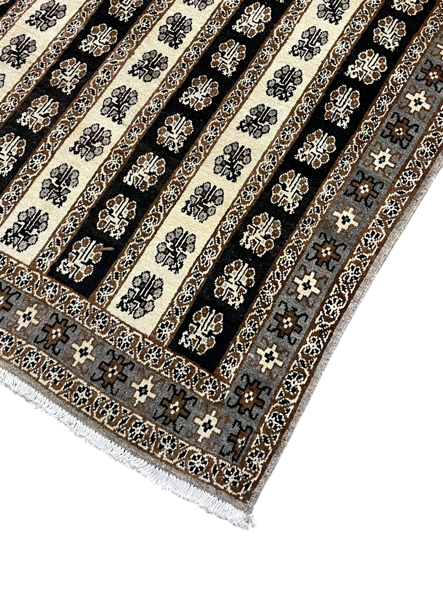 Persian ivory ground rug, the field divided into stripes decorated with stylised flower heads, the border with repeating cross motifs within guard stripes 