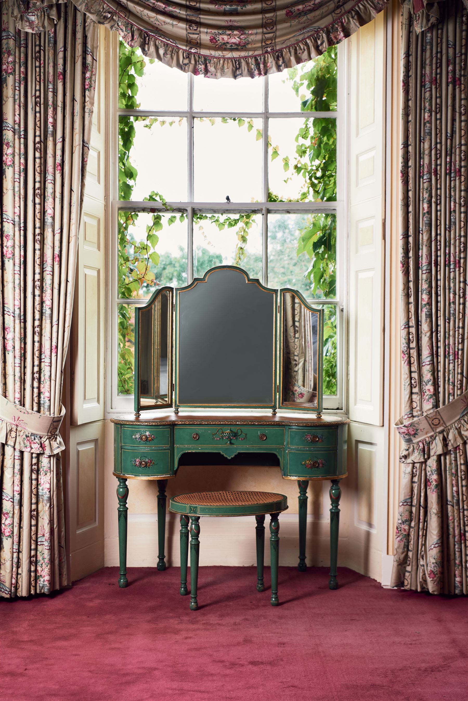 Edwardian Adam Revival green-painted and parcel gilt kidney-shaped dressing table, raised triple mirror back with shaped cresting, leather inset top within a trailing floral painted band and foliate carved edge, fitted with five drawers decorated with urn and floral bouquets, on turned supports painted with acanthus leaves and draped festoons; together with matching stool with cane seat 