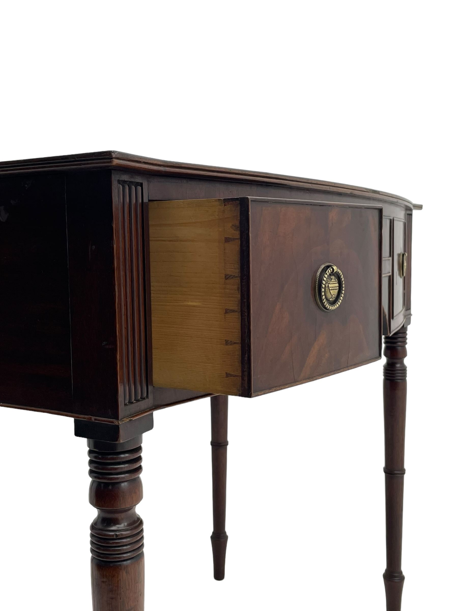 George III mahogany kneehole dressing or writing table, stepped bow-front form, reed moulded top with mahogany crossband, fitted with three cock-beaded drawers with circular pressed brass handle plates decorated with urn and beaded ring handle, on ring turned supports 