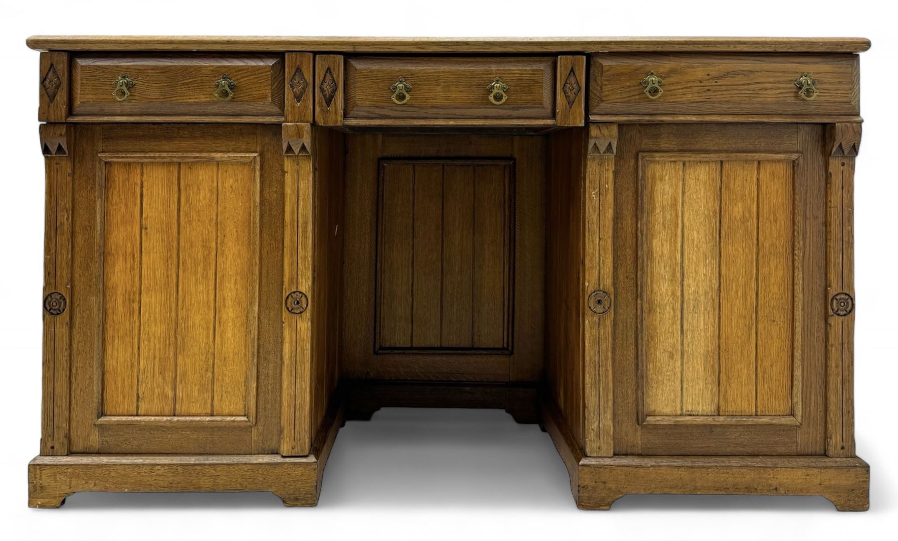 Late Victorian oak twin pedestal desk, chamfered rectangular top over three convex front edge drawers and two panelled cupboards, flanked by carved supports with roundels and diamond motif, on bracketed plinth base