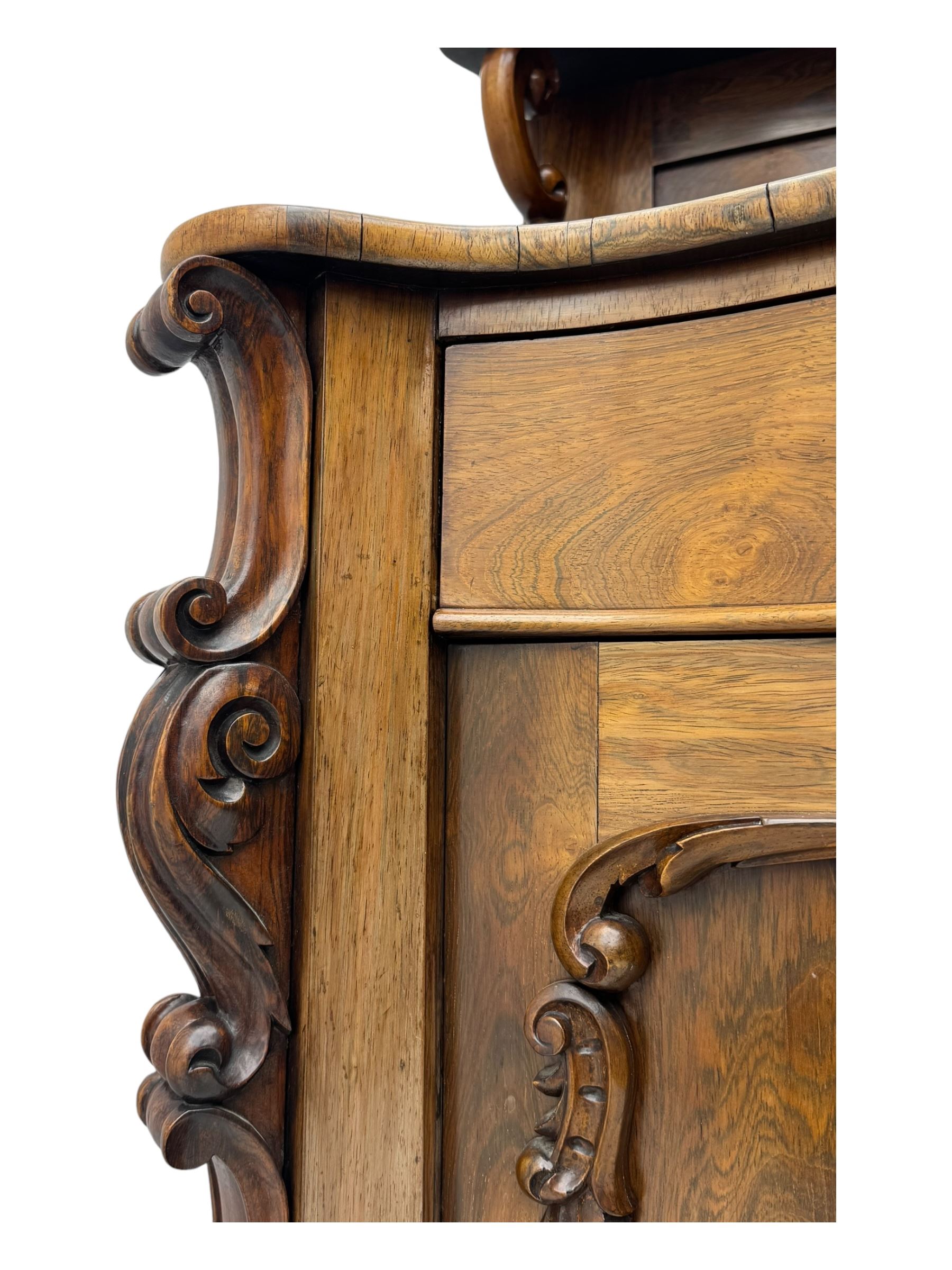 Mid-19th century rosewood chiffonier, raised back with scroll and leaf carved shaped pediment, serpentine top over drawer and double cupboard with scrollwork decoration, on shaped plinth base