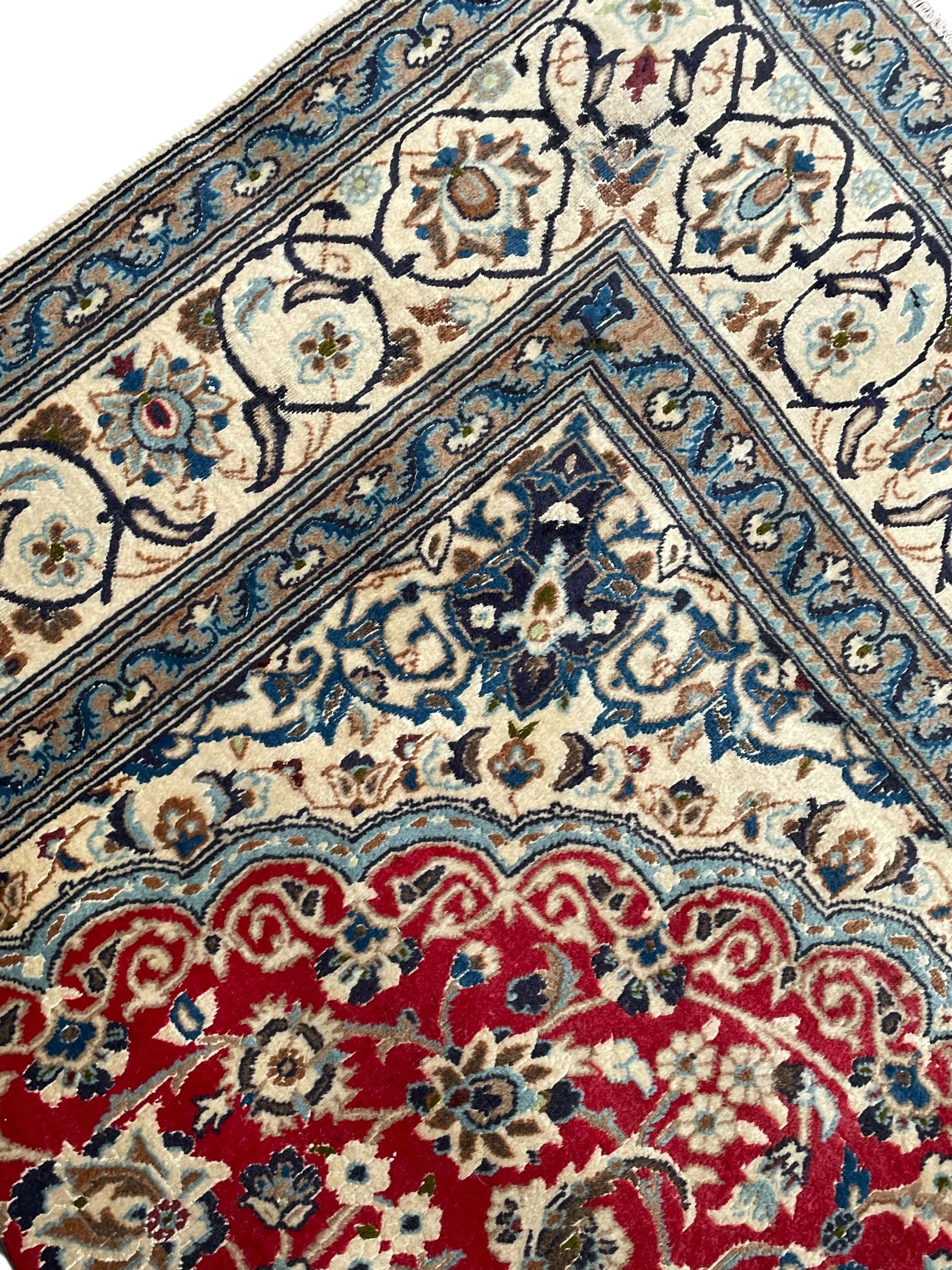 Persian Kashan crimson rug, central cusped medallion surrounded by interlacing branches decorated with leaves and palmettes, ivory ground spandrels and border decorated with scrolling branches and stylised plant motifs, within guard stripes  