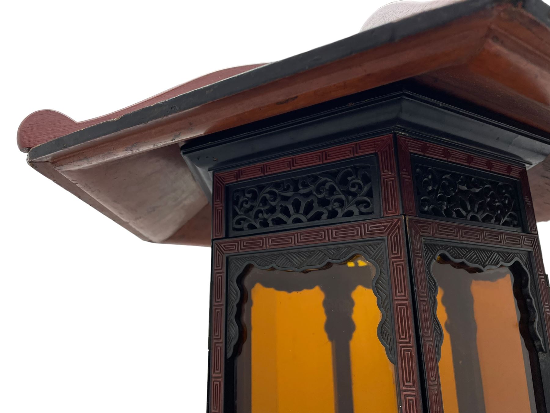 20th century Chinese black and red lacquered hardwood lantern stand, hexagonal shaped canopy top carved with flower heads and scrolls, the lantern fitted with amber tinted glass panes, pierced and carved upper panels, enclosed by two hinged doors, turned stem carved in relief with trailing vine leaves with fruits, stepped hexagonal base with carved decoration  