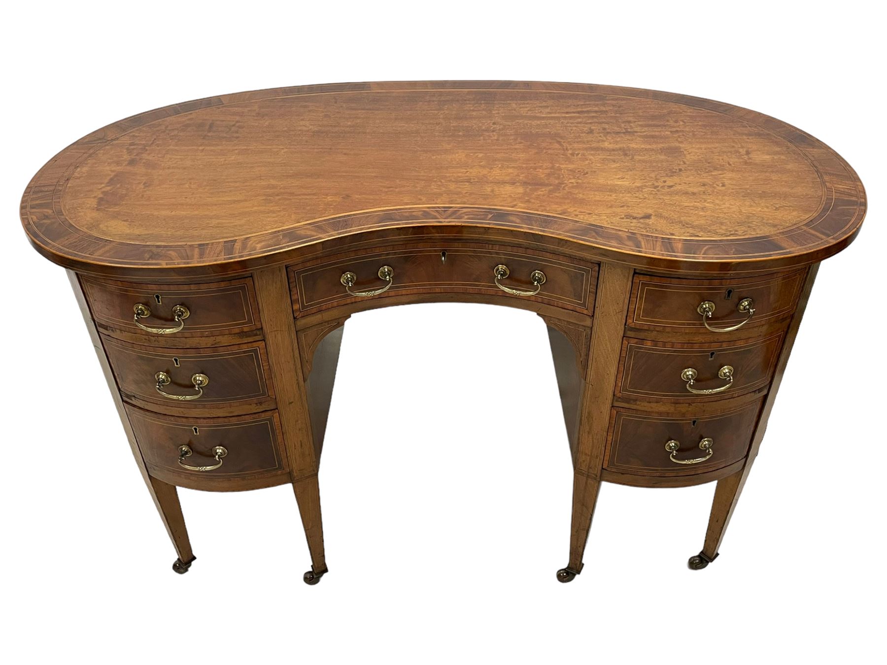 Edwardian mahogany and satinwood banded kidney-shaped writing desk, the shaped top with figured mahogany banding and boxwood stringing, fitted with seven drawers with satinwood bandings, on square tapering supports with brass and ceramic castors