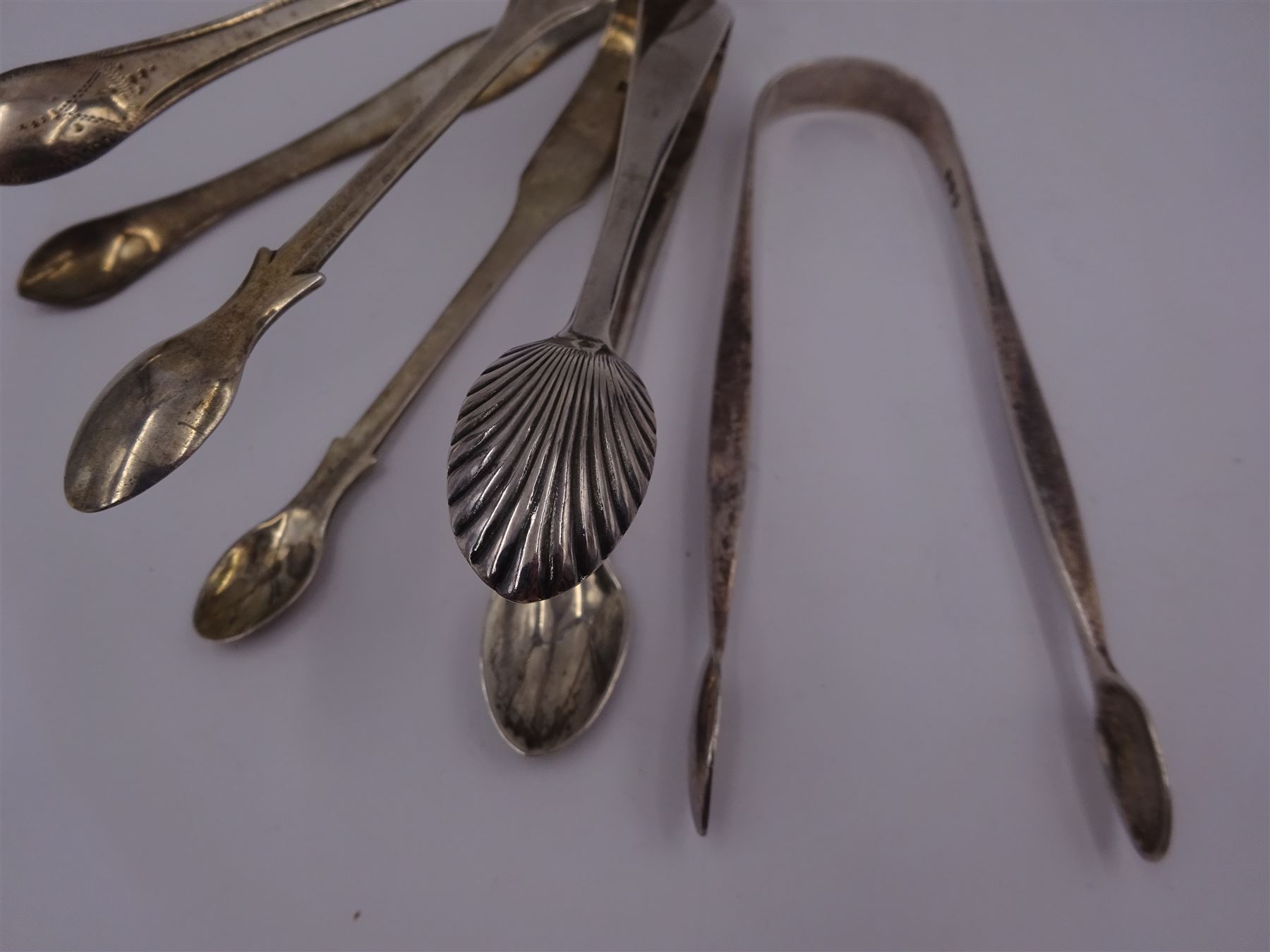 Four pairs of silver sugar tongs, to include three George III pairs comprising a bright cut engraved example, hallmarked Peter, Ann & William Bateman, London 1801, a fiddle pattern example, with engraved initials, hallmarked Thomas Wallis II, London 1806 and one other, hallmarked Stephen Adams II, London 1800, together with an Edwardian pair, with shell bowls, hallmarked Mappin & Webb Ltd, Sheffield 1909