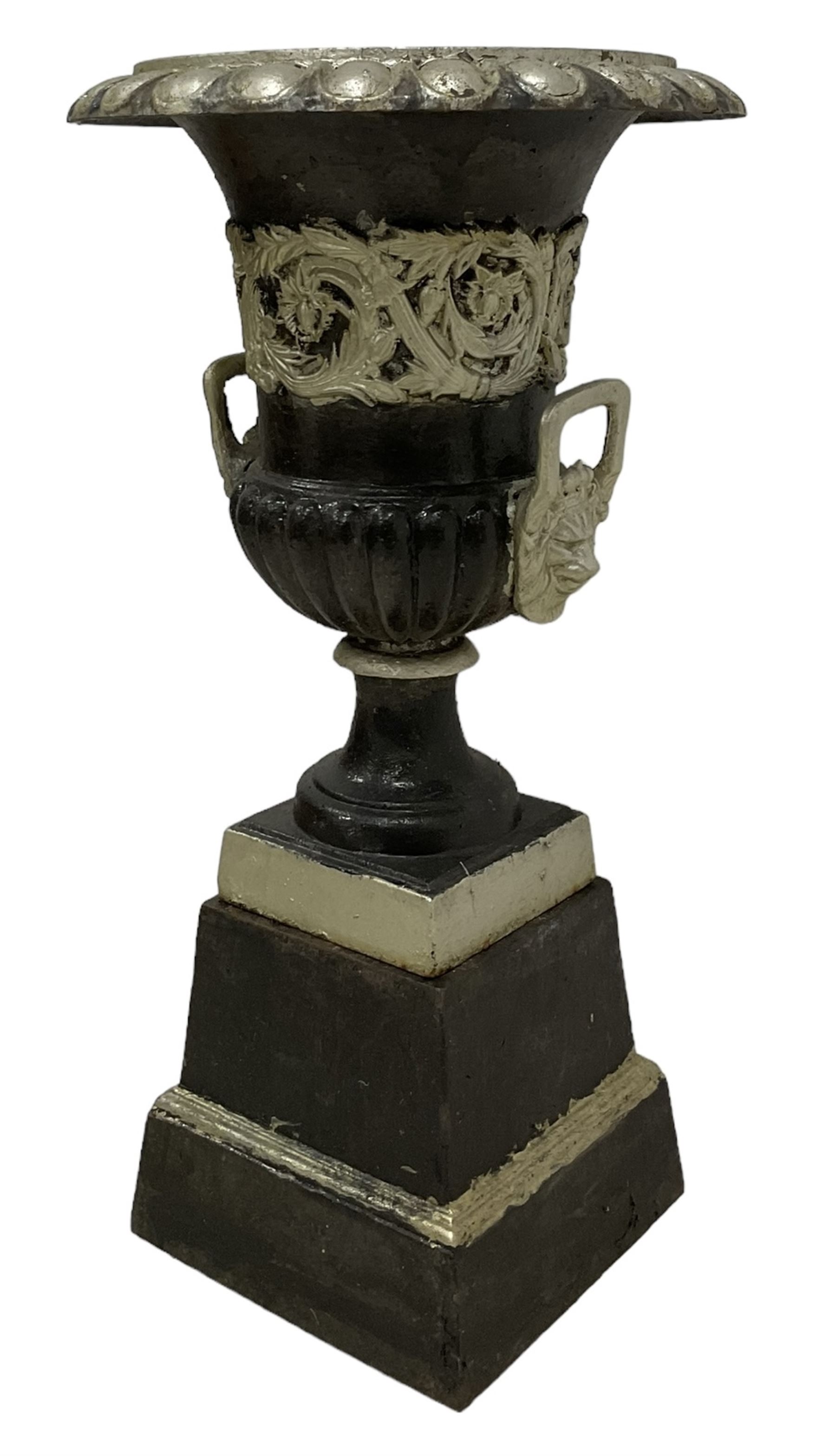 20th century cast iron Campana-shaped urn on plinth, with scrolling foliate relief decoration, in ebonised and silver painted finish