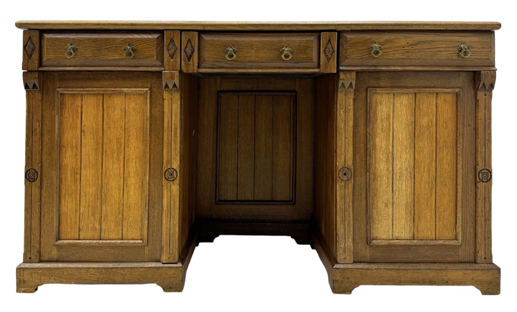 Late Victorian oak twin pedestal desk, chamfered rectangular top over three convex front edge drawers and two panelled cupboards, flanked by carved supports with roundels and diamond motif, on bracketed plinth base