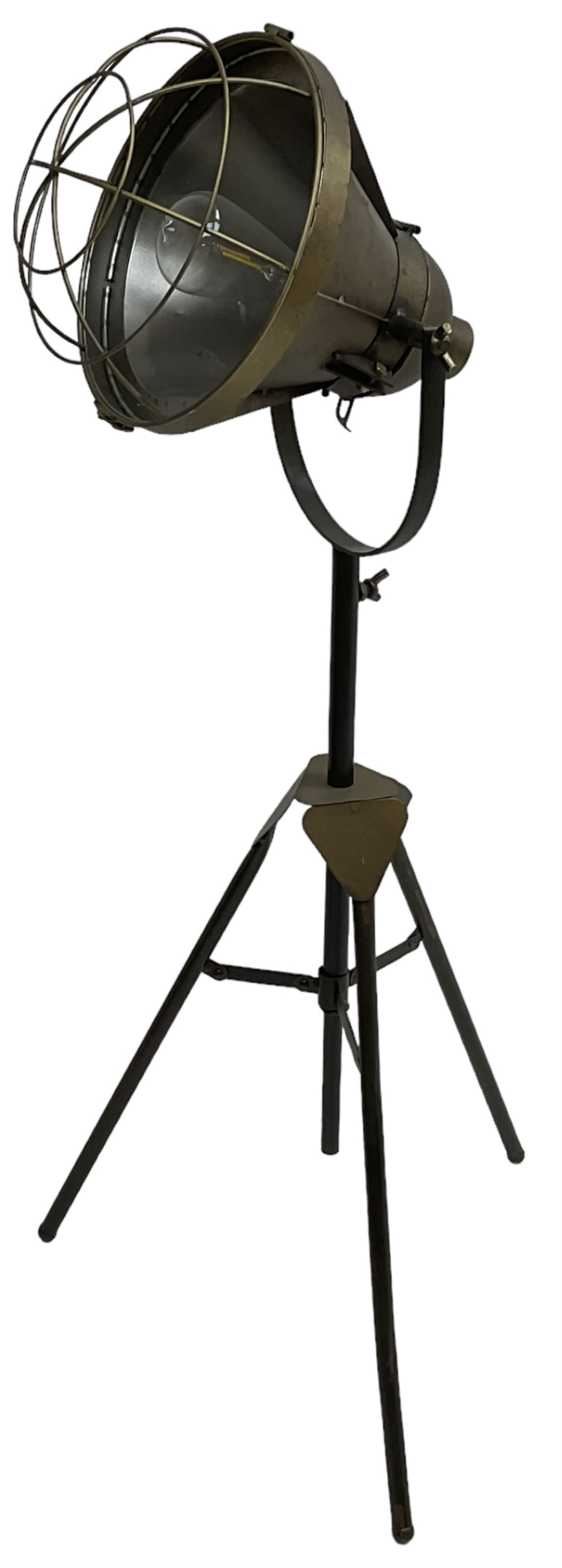 Industrial tripod spotlight, with a metal shade and wire guard, supported by a height-adjustable tripod base, the head equipped with an adjustable tilt mechanism