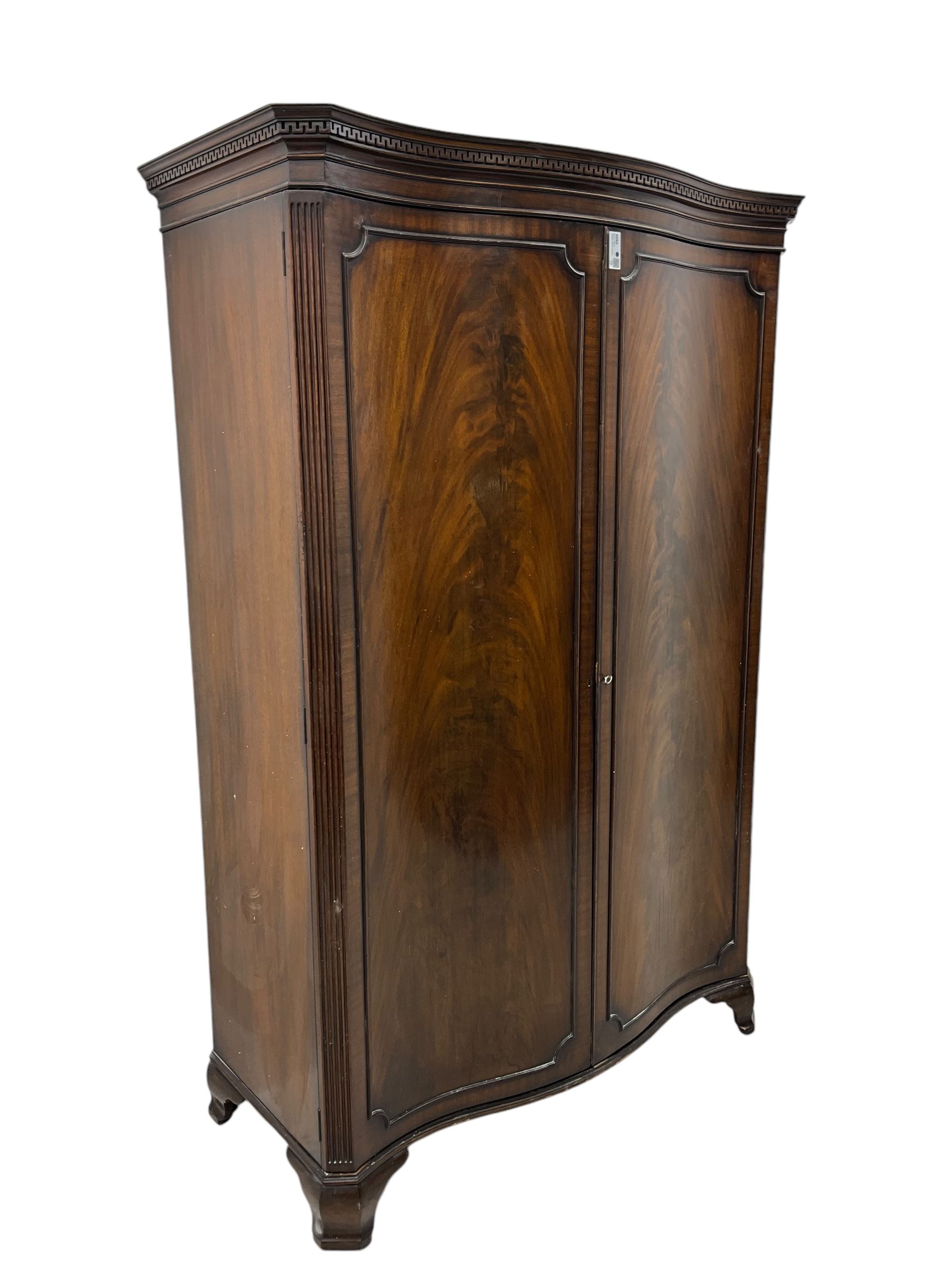 Early 20th century mahogany serpentine double wardrobe, moulded cornice over two figured doors, the interior fitted with hanging rail and shelf, canted and fluted uprights, on bracket feet 