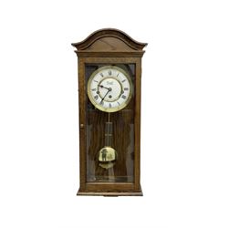 Commiti of London -  three train spring driven 8-day wall clock in an oak case, with a fully glazed door and curved pediment, two part dial with Roman numerals, spade hands and gridiron pendulum, rack movement chiming the hours and quarters on 5 gong rods. With key.