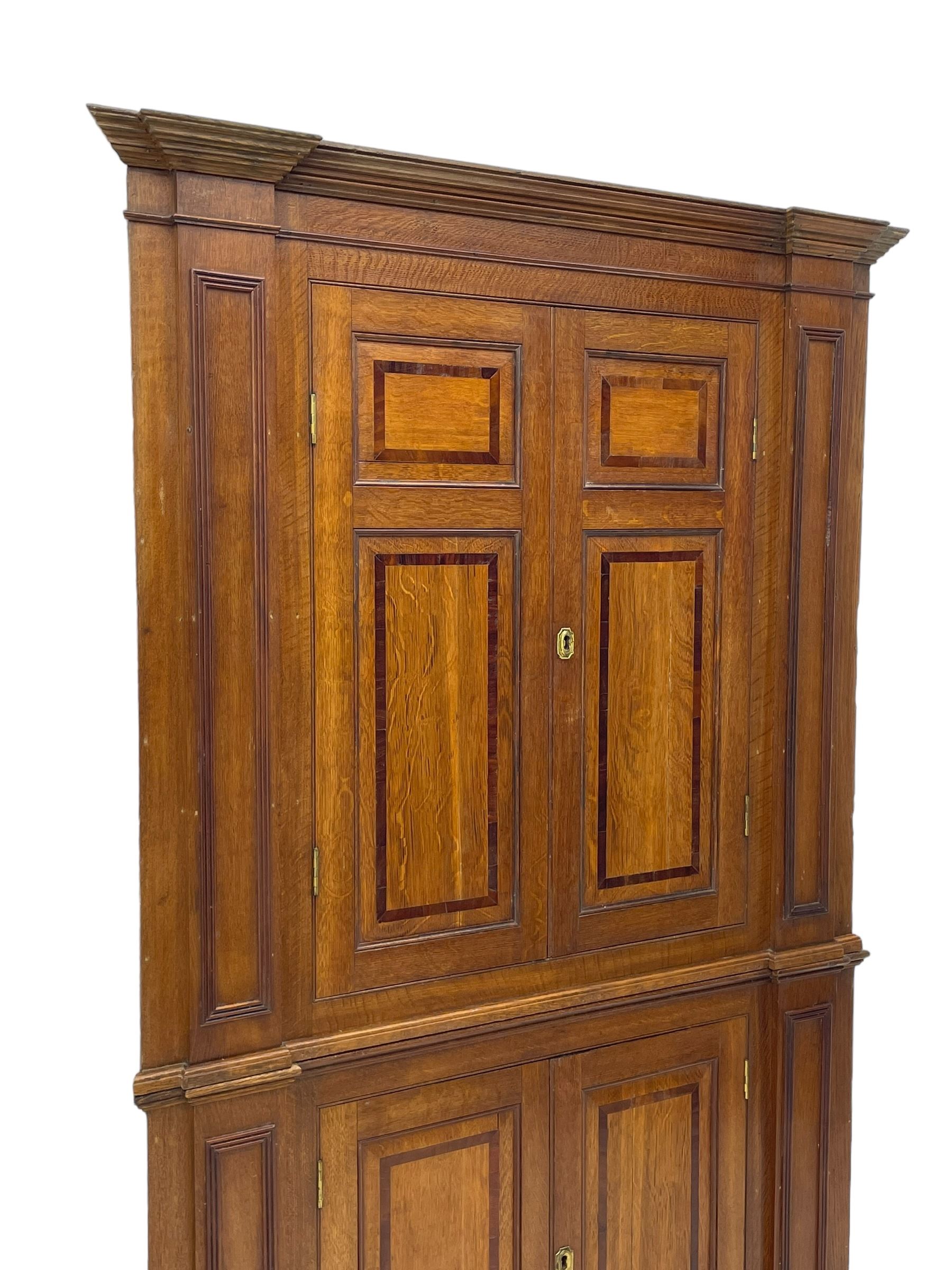 George III and later oak and mahogany banded corner cupboard, moulded cornice over four panelled doors, the door panels inlaid with mahogany bands, projecting square pilasters throughout with applied reeded mouldings, the painted interior fitted with shaped shelves, on moulded plinth base 