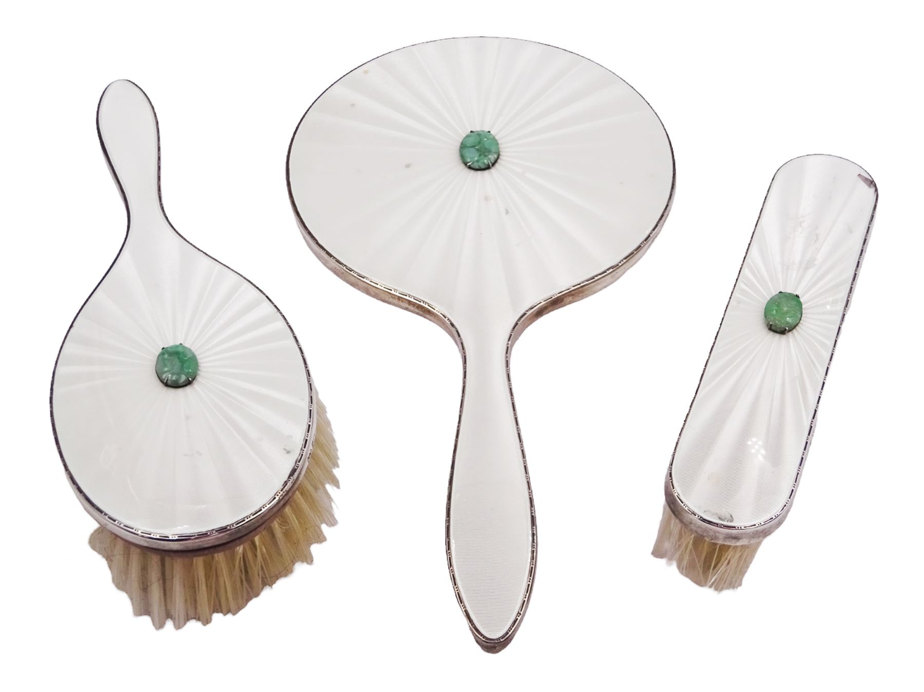 Mid 20th century silver mounted three piece dressing table set, comprising hand mirror, hair brush and clothes brush, each with white guilloche enamel decoration and set with a carved green hardstone, hallmarked Henry Clifford Davis, Birmingham 1959