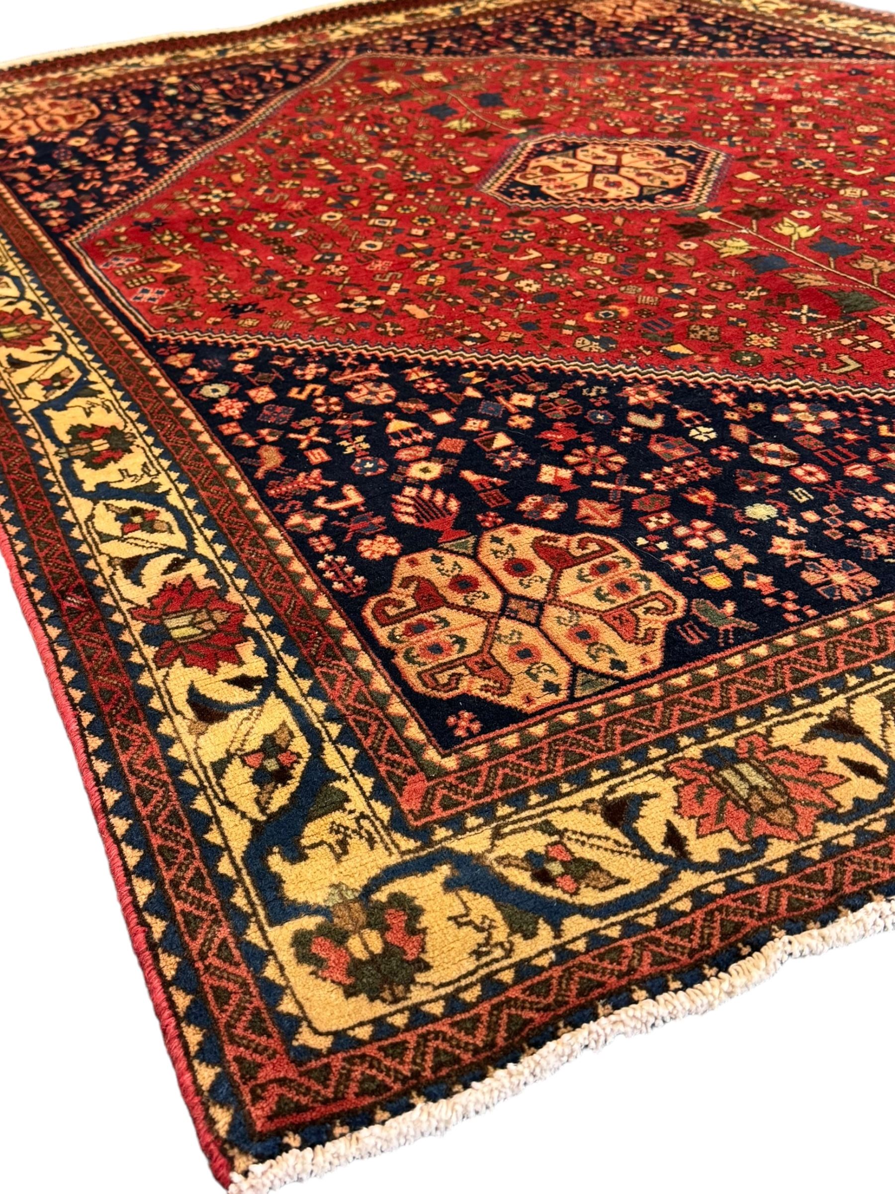 South West Persian Abadeh crimson ground rug, indigo ground with crimson lozenge field, decorated all over with small stylised motifs of flowerheads, hooks, animals and birds, guarded border decorated with trailing leaves and stylised plant motifs 