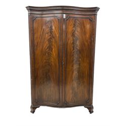 Early 20th century mahogany serpentine double wardrobe, moulded cornice over two figured doors, the interior fitted with hanging rail and shelf, canted and fluted uprights, on bracket feet 