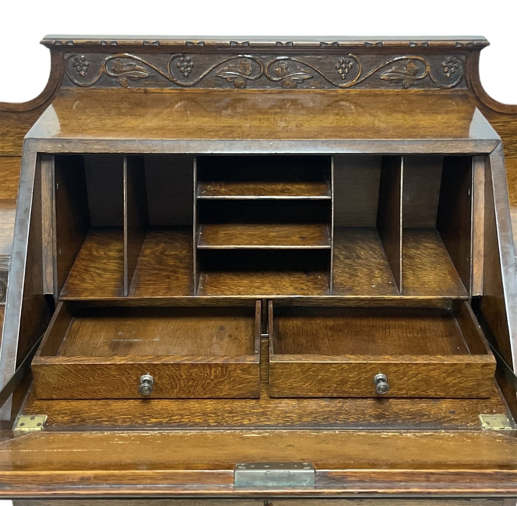 Early 20th century heavily carved oak bookcase bureau, raised back with grape-vine carved frieze, over fall-front enclosing fitted interior, above two short drawers and curved frieze drawer, flanked by astragal glazed and panelled cupboards, on turned feet