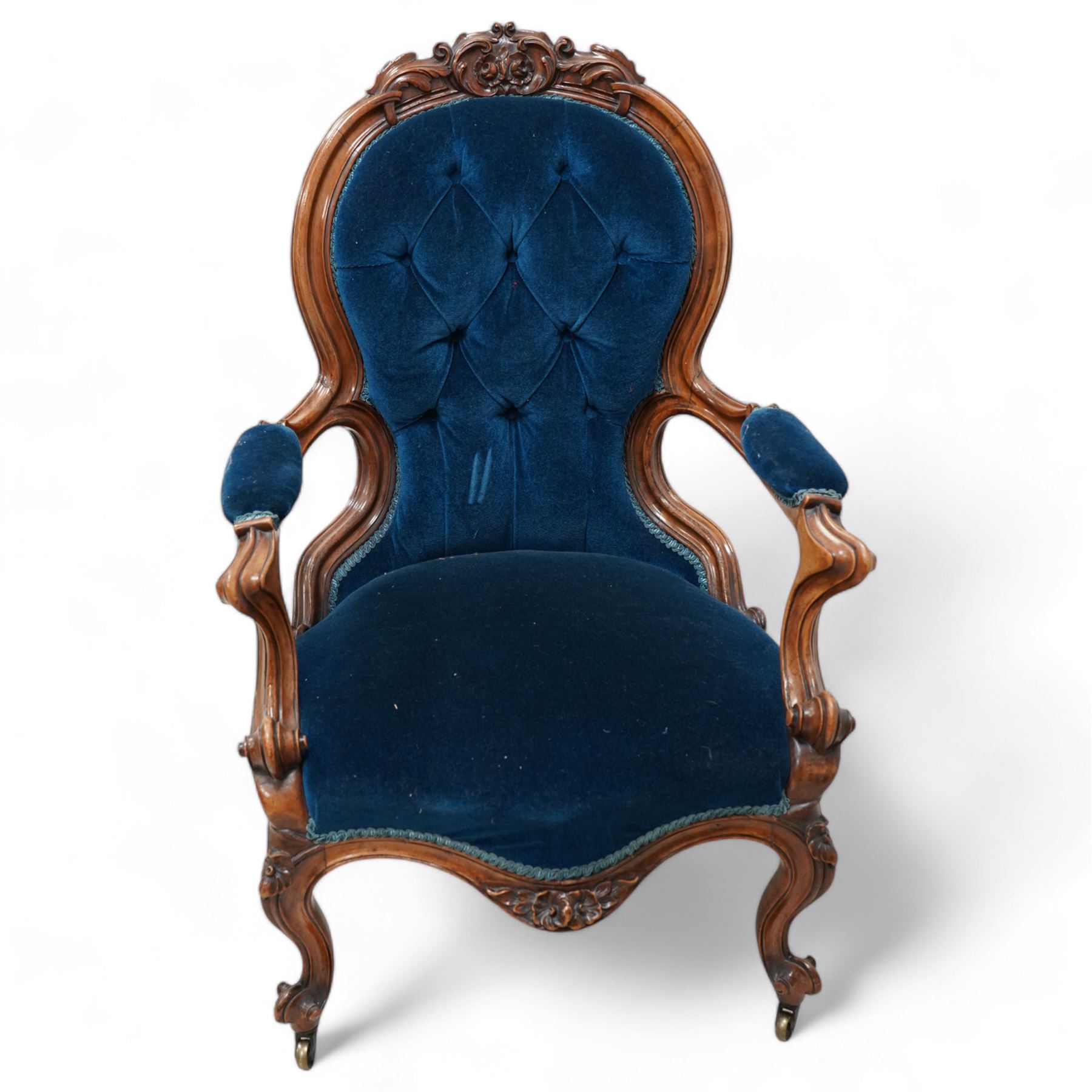 Victorian walnut framed open armchair, curled leaf carved cresting rail over scrolled and shaped arms, upholstered in buttoned blue velvet fabric, on cabriole feet