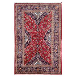 Persian Kashan crimson ground rug, overall arabesque design, the field decorated with swirled leafy branches and palmettes, indigo ground border decorated with repeating pattern, within guard stripes 