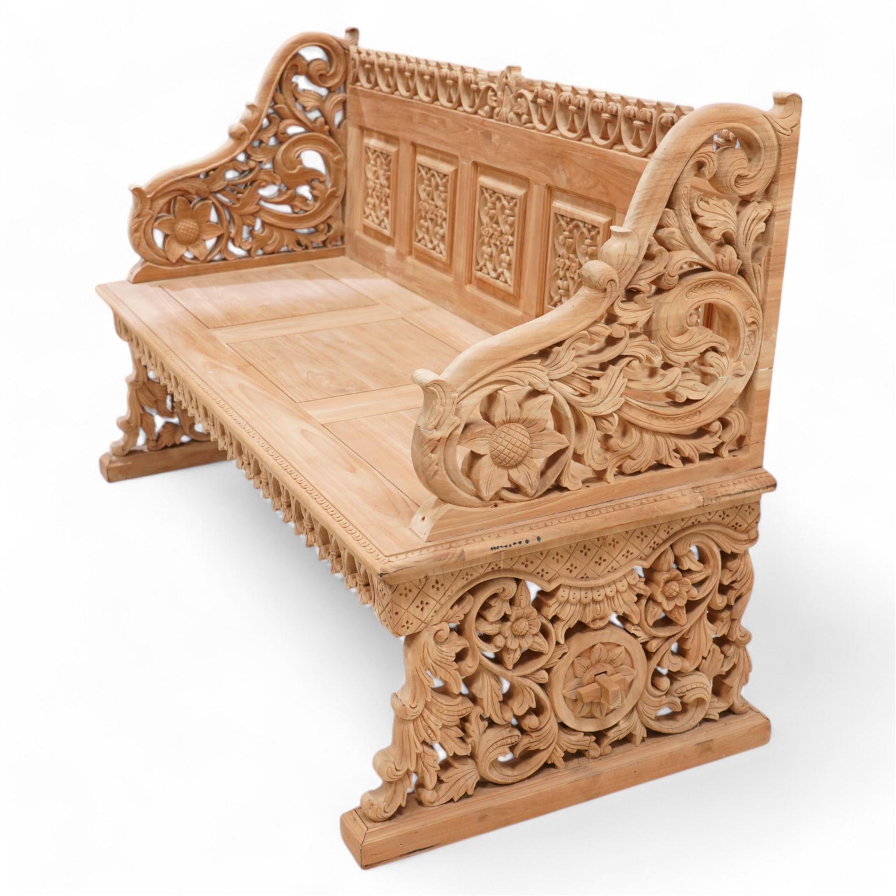 Hand carved teak garden bench, C-scroll and foliate carved cresting rail over four pierced and flower head carved panels, shaped and scrolling end supports carved with flower heads and curling leafy branches, united by pegged stretcher