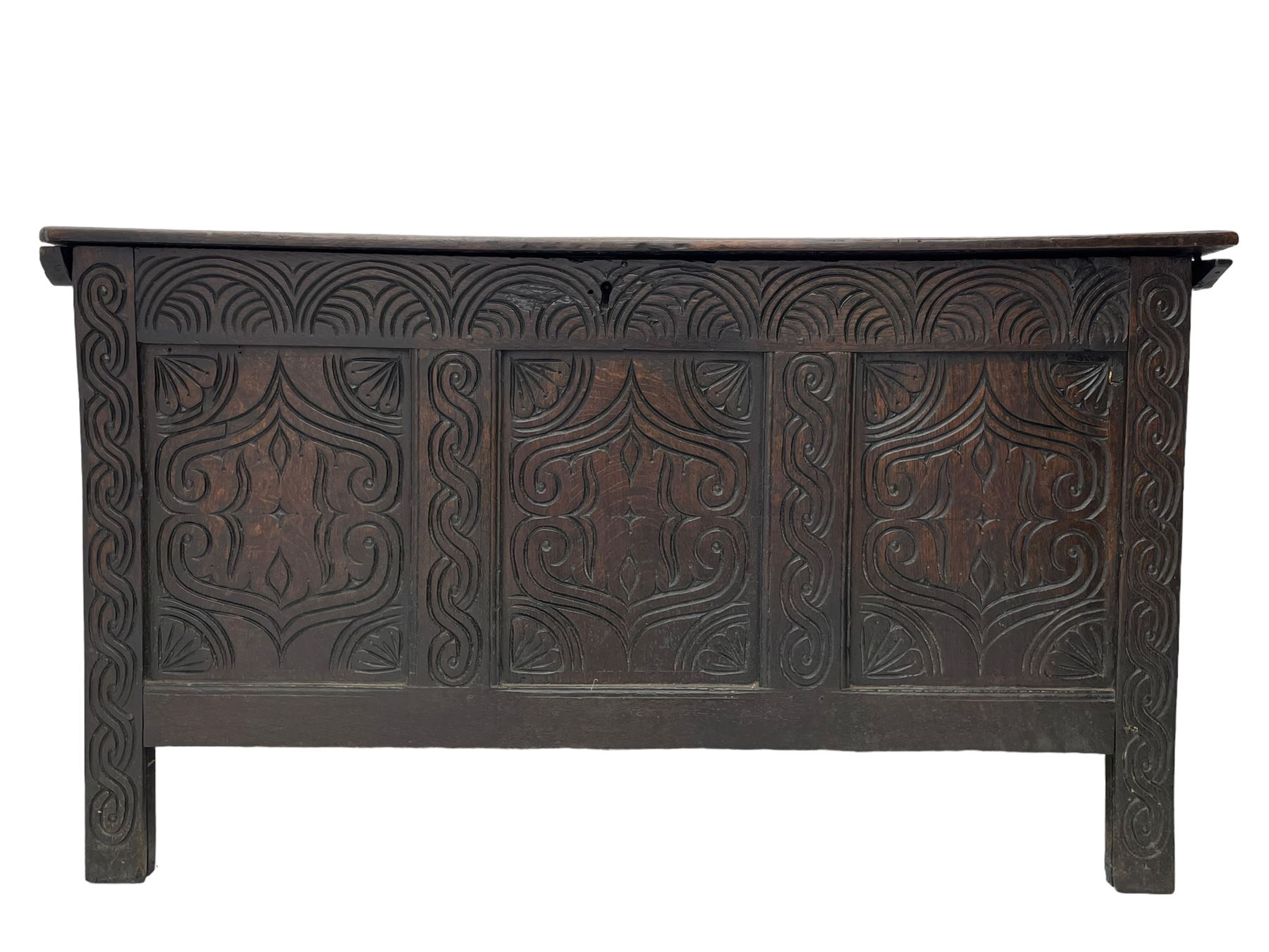 18th century oak blanket box, moulded and chip carved hinged lid, lunette carved cresting rail over triple panelled front carved with stylised leaf and scroll decoration, interlocking S-scroll carved upright rails, panelled sides and back, on stile supports 