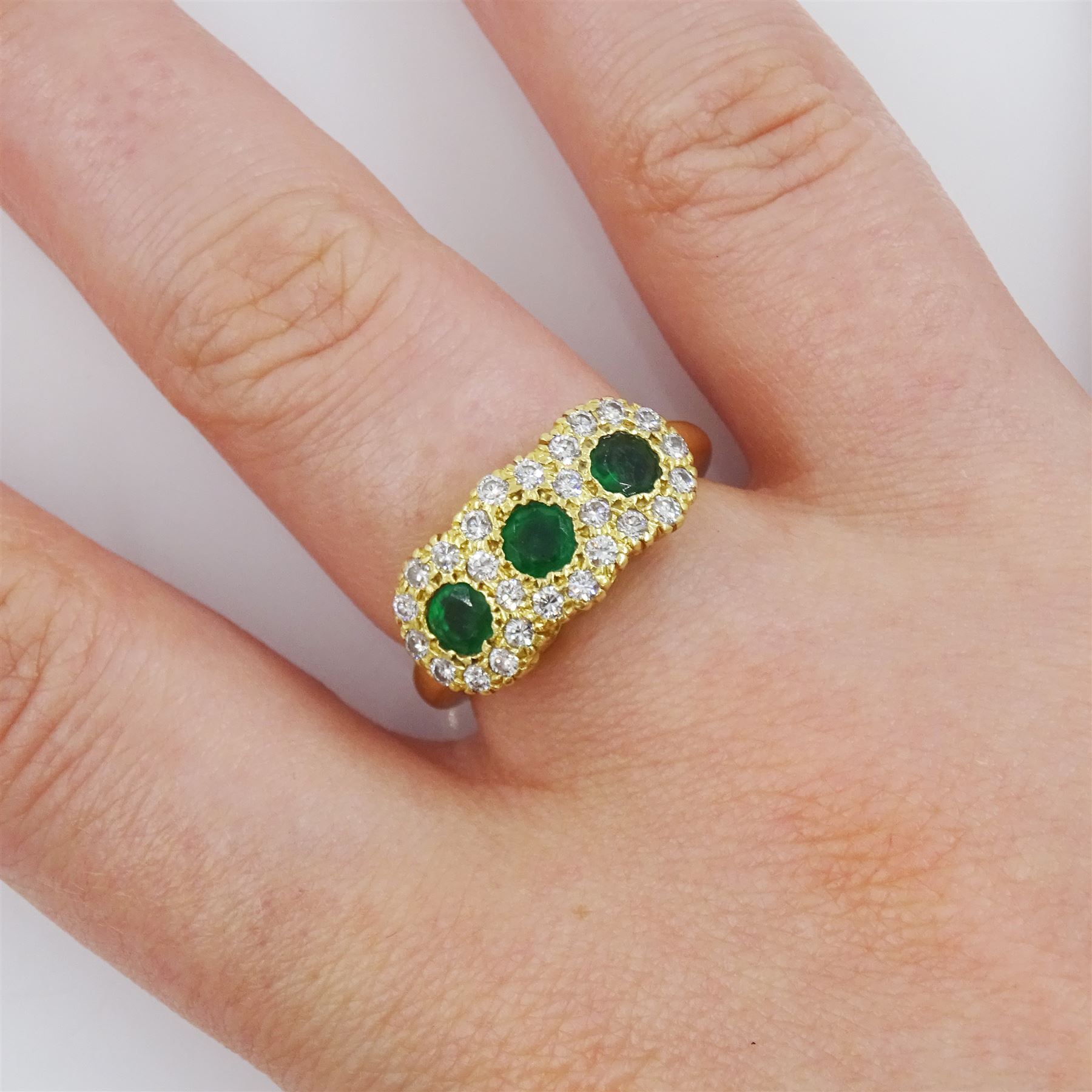 18ct gold emerald and diamond cluster ring, three round cut emeralds, with round brilliant cut diamond surround, London 1976