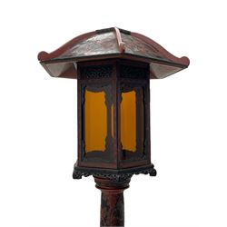 20th century Chinese black and red lacquered hardwood lantern stand, hexagonal shaped canopy top carved with flower heads and scrolls, the lantern fitted with amber tinted glass panes, pierced and carved upper panels, enclosed by two hinged doors, turned stem carved in relief with trailing vine leaves with fruits, stepped hexagonal base with carved decoration  