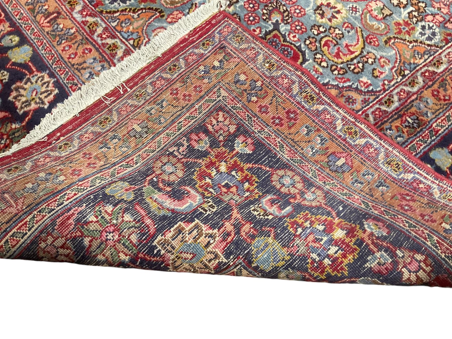 Large Persian Kashan crimson ground carpet, the busy field decorated with a central floral pole medallion surrounded by stylised plant motifs and palmettes with contrasting indigo spandrels, the guarded border decorated with repeating connected foliate designs