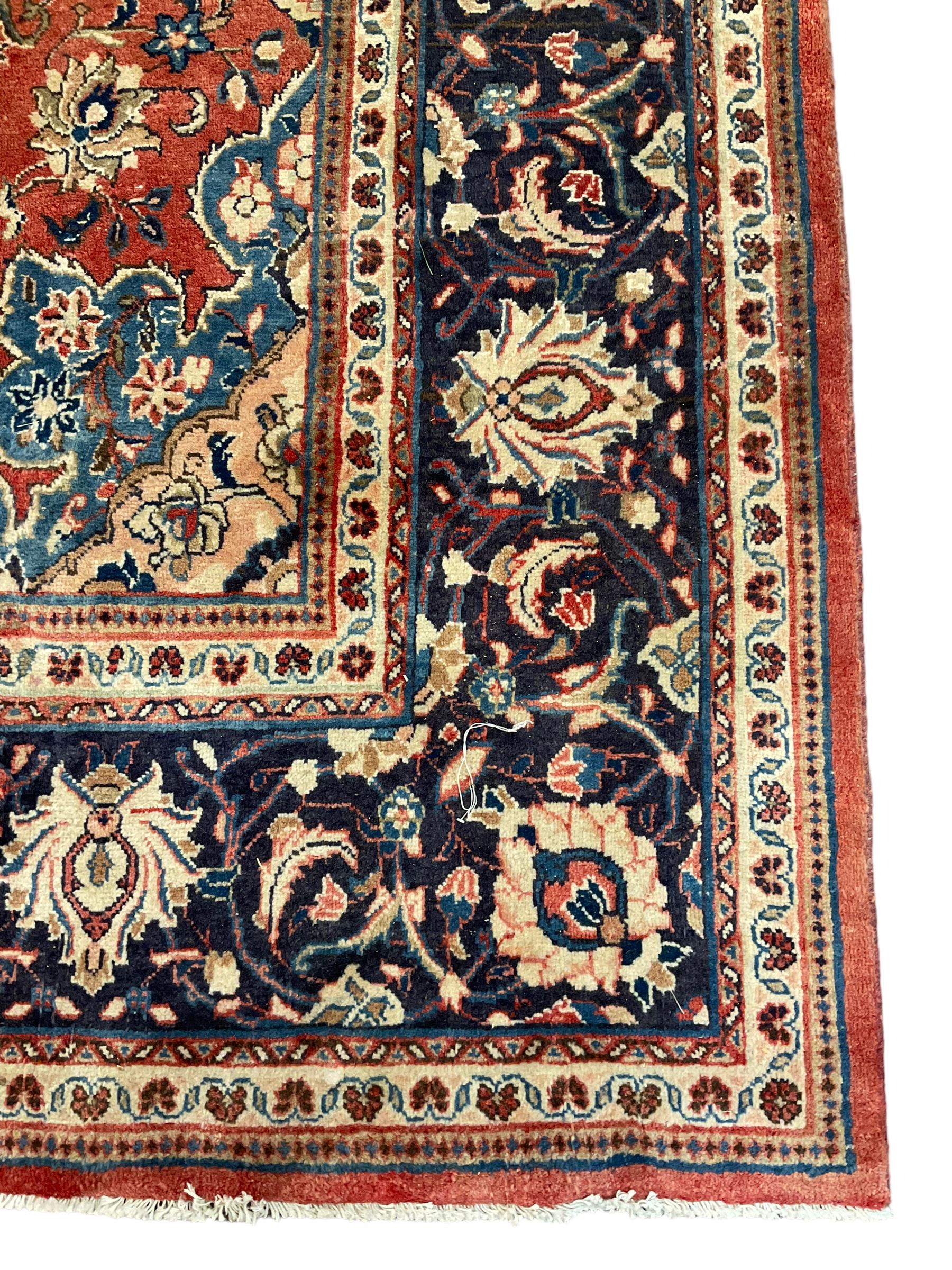 Persian Kashan crimson ground carpet, central shaped pale ground medallion surrounded by interlacing branches and stylised floral motifs, indigo main border with scrolling foliage design, within guard stripes 