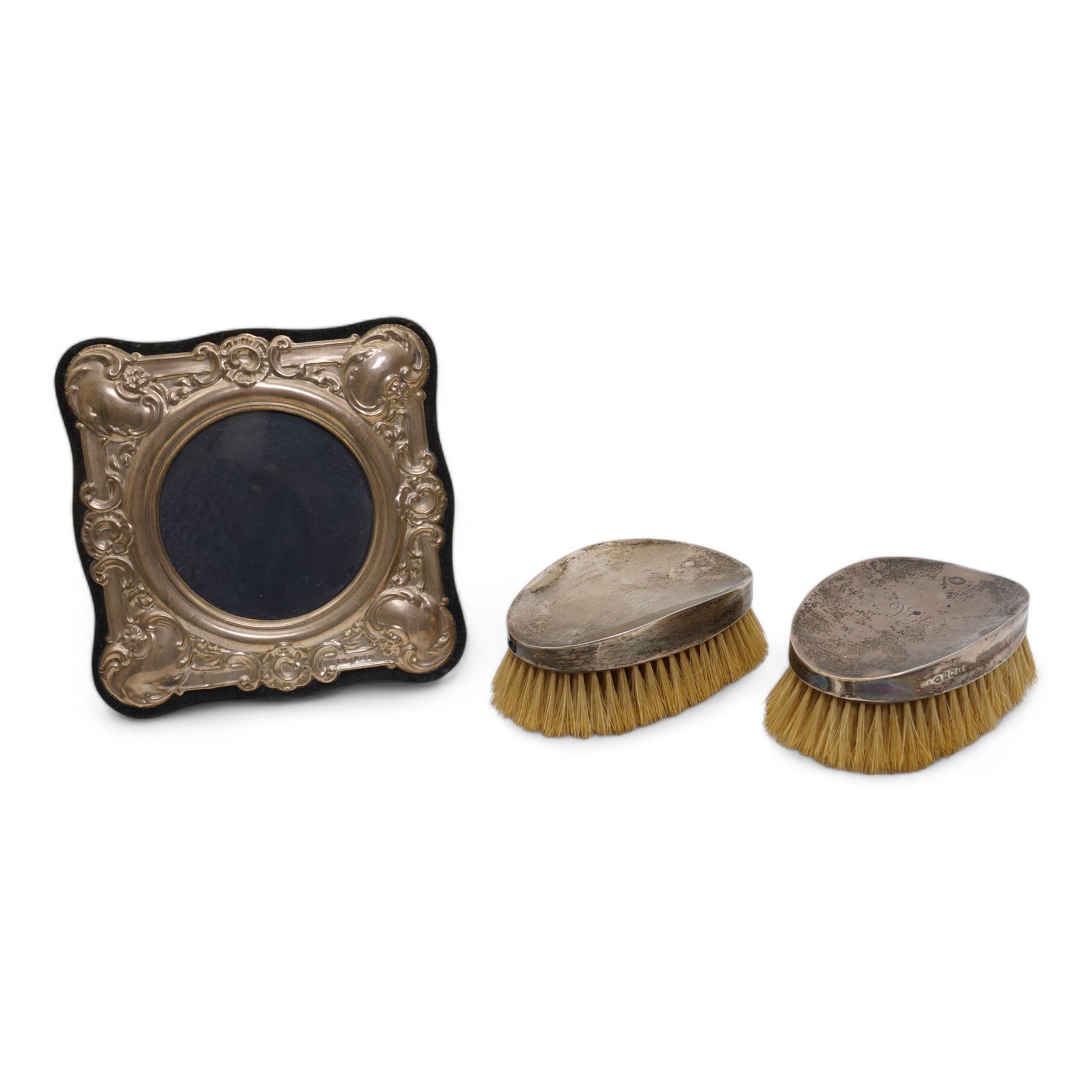 Silver photograph frame with embossed decoration and circular aperture D10cm Birmingham 1984 and a pair of silver backed gentleman's hair brushes Birmingham 1922