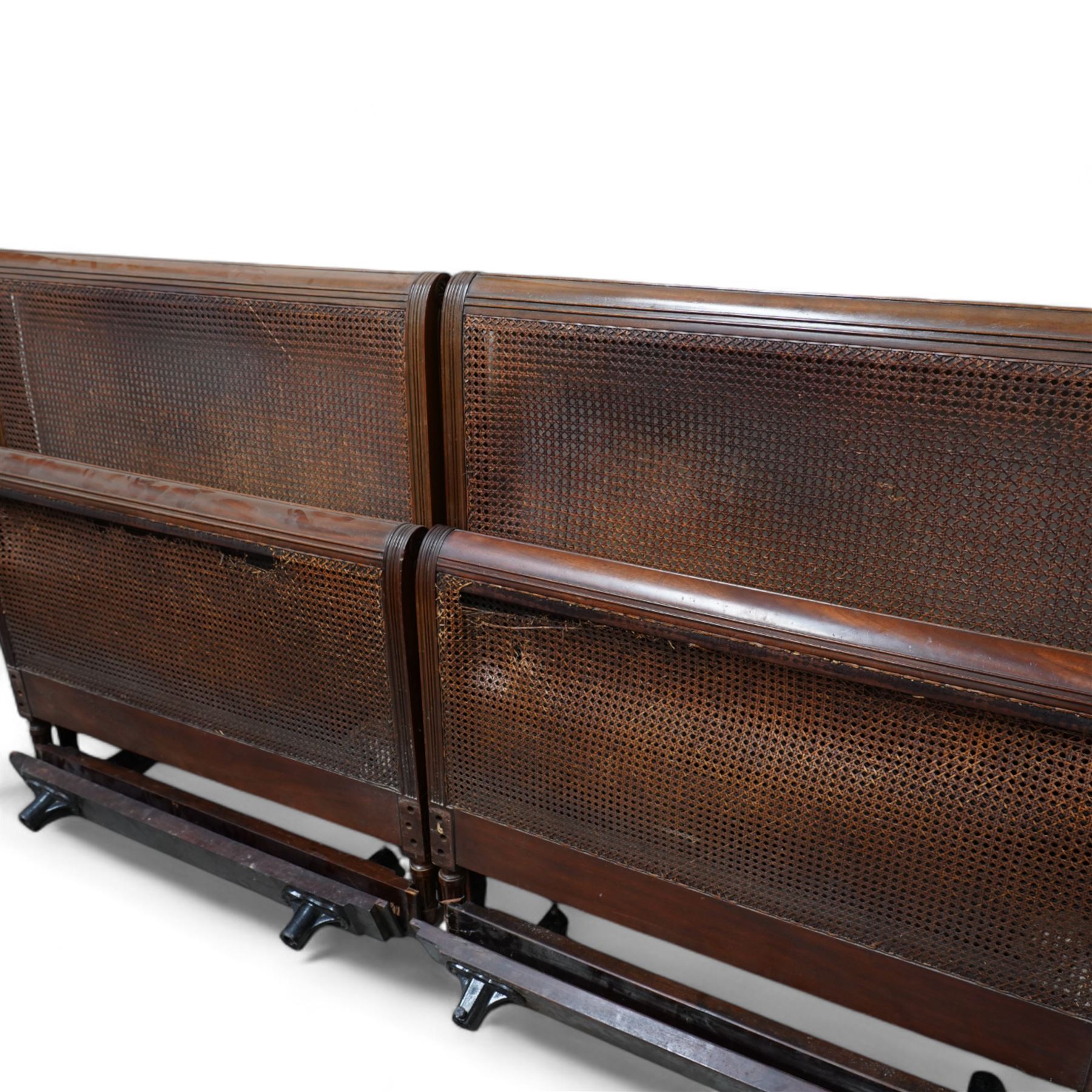 Heal's of London - pair of early 20th century mahogany bergère single beds, rolled head and footboards with moulded frames and canework panels, carved with flower head motifs, on turned and fluted feet, upholstered bed bases