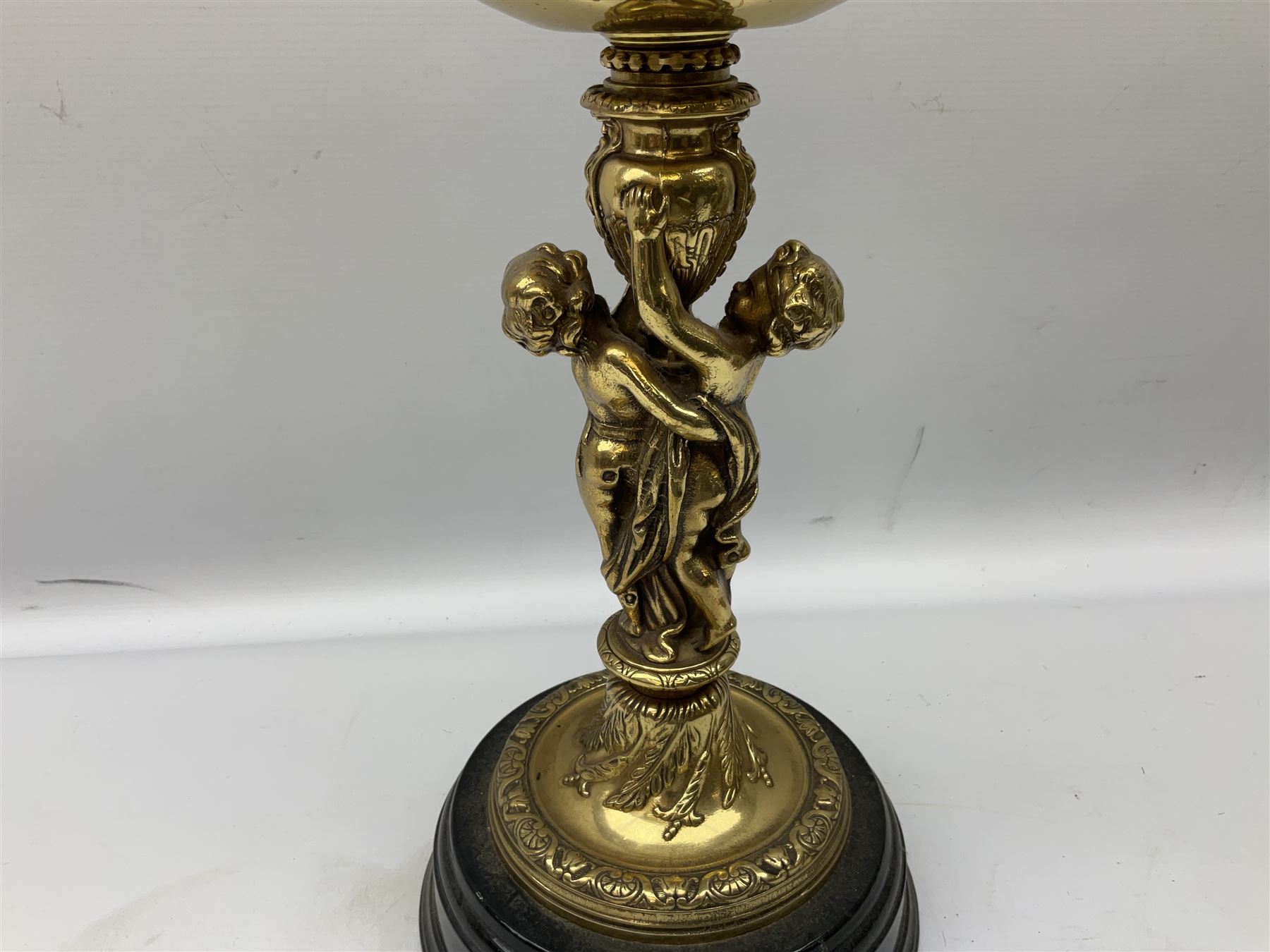 Late 19th/early 20th century brass oil lamp, the central column modelled with two cherubs, supporting the reservoir with wyrthen twist etched floral shade, raised upon circular base