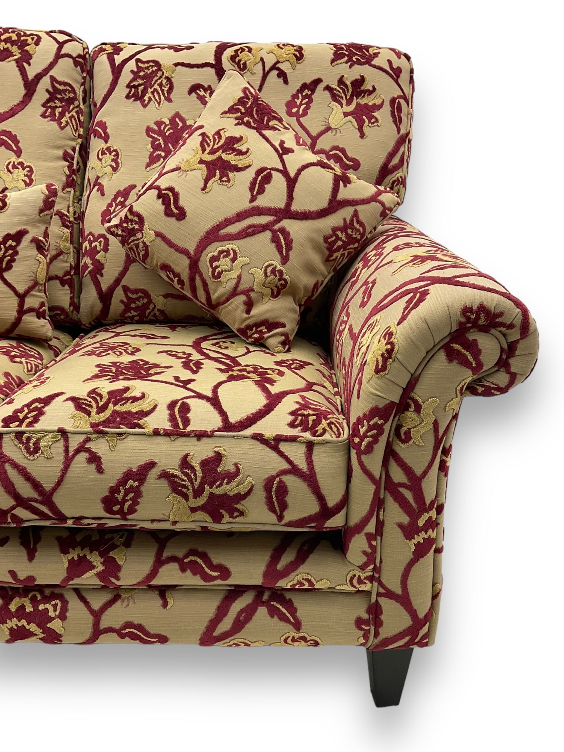 Contemporary upholstered three-seat sofa, scroll arms and loose cushions, embossed beige ground fabric with red and gold floral motifs, on tapered wooden supports