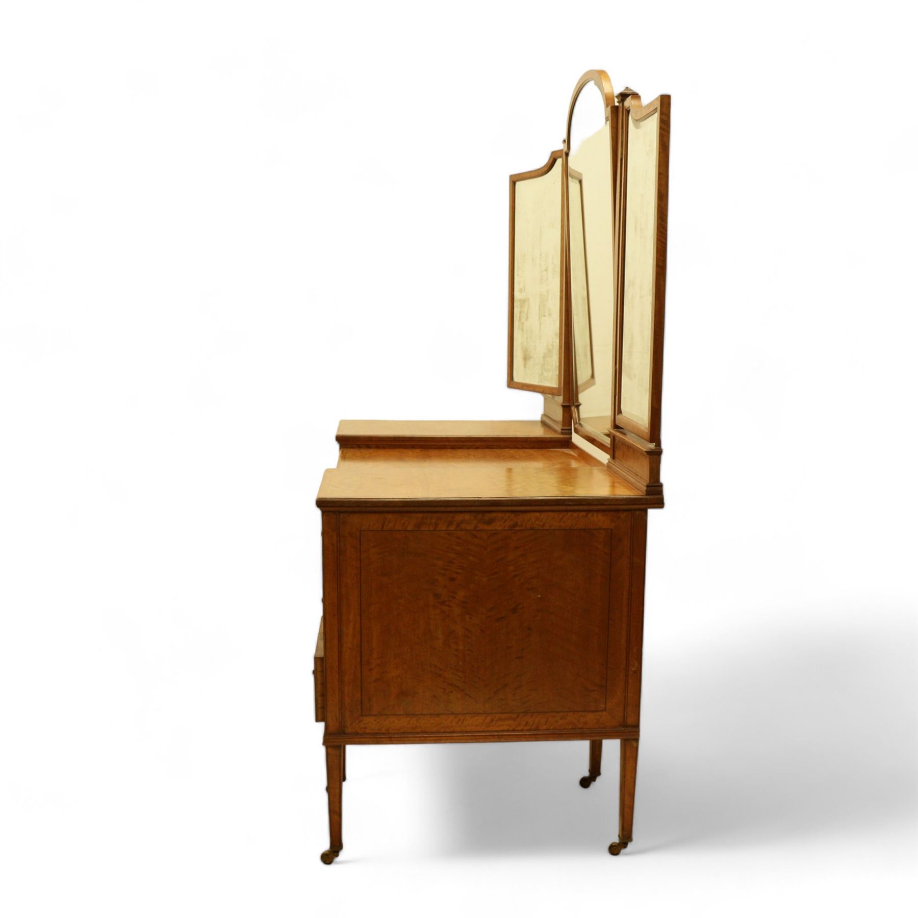 Waring & Gillow Ltd. - Edwardian satinwood dressing table, raised bevelled triple mirror back on square supports, over frieze inlaid with geometric stringing in ebony, moulded drop-centre table with stringing, fitted with seven drawers, reeded and foliate cast handles and square leaf cast handle plates, on square tapering supports terminating to brass castors, the centre drawer with metal maker's plaque and maker's stamp for 'Waring & Gillow, Ltd.', the top three drawers fitted with Chubb locks, the remaining drawers fitted with locks stamped 'Gillows Lancaster', together with associated chair 